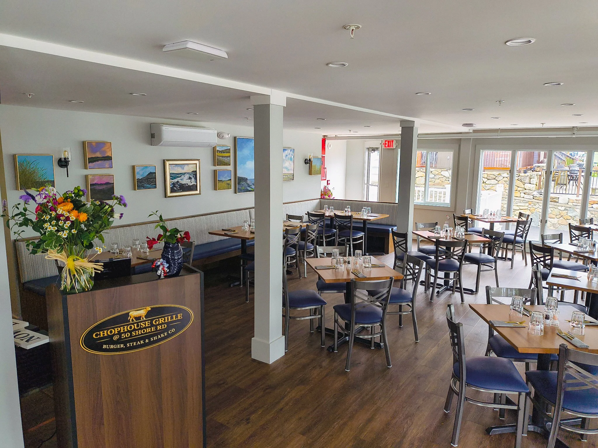 Interior view of a restaurant with tables set for dining, artwork on the walls, and windows letting in natural light.
