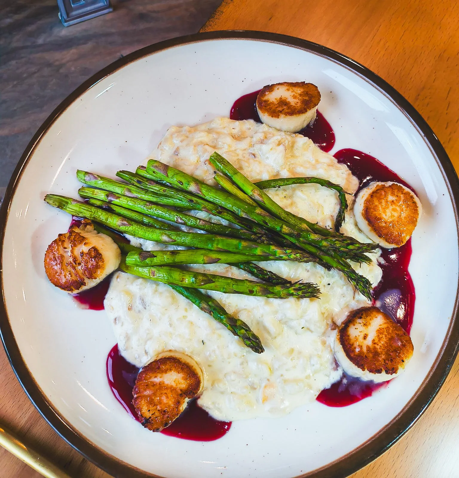 A plate of breakfast food including five scallops, roasted asparagus, and a fluffy egg dish with a red berry sauce.