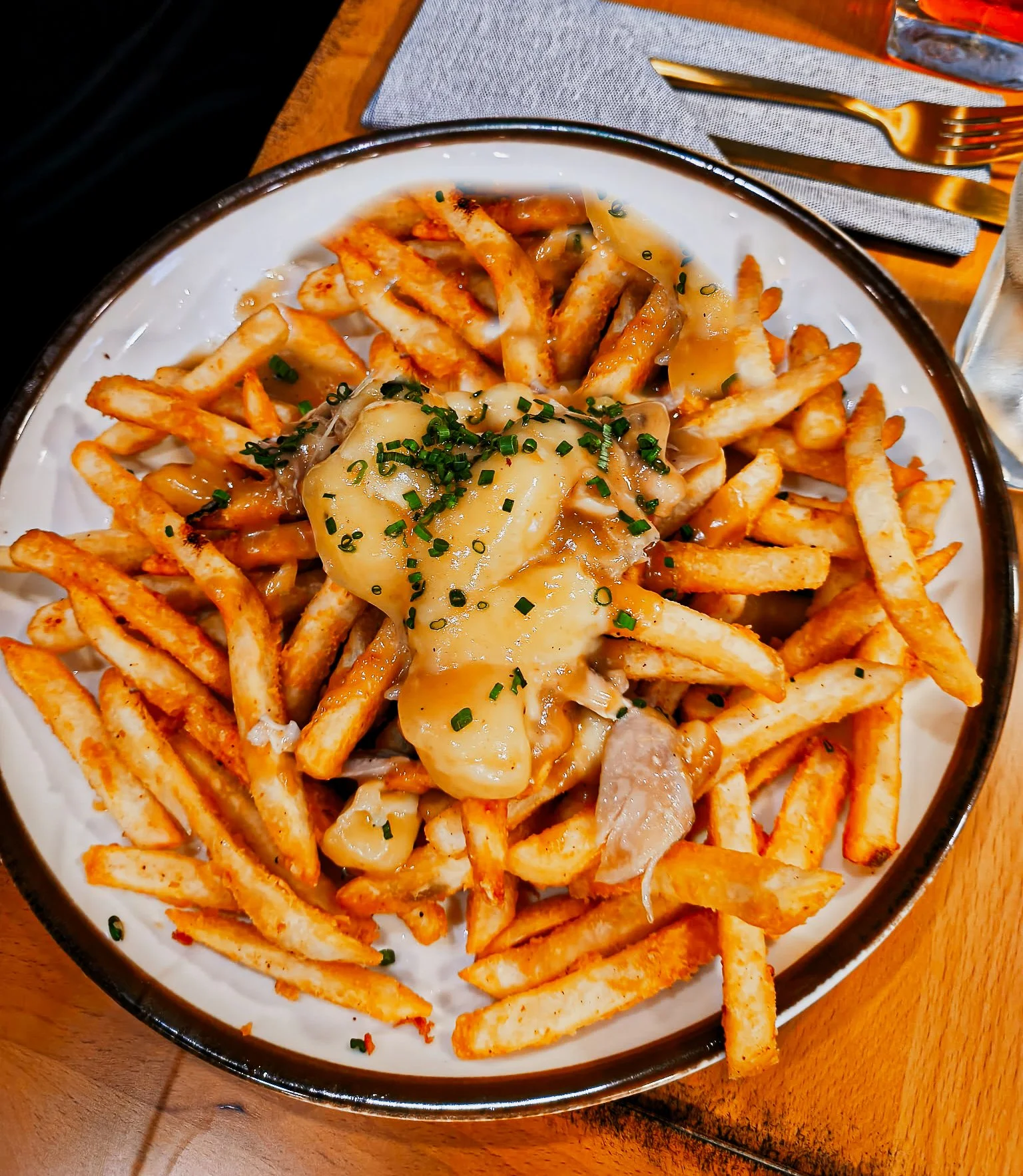 Plate of French fries topped with cheese, gravy, and chopped herbs, served with a side of fried chicken pieces.