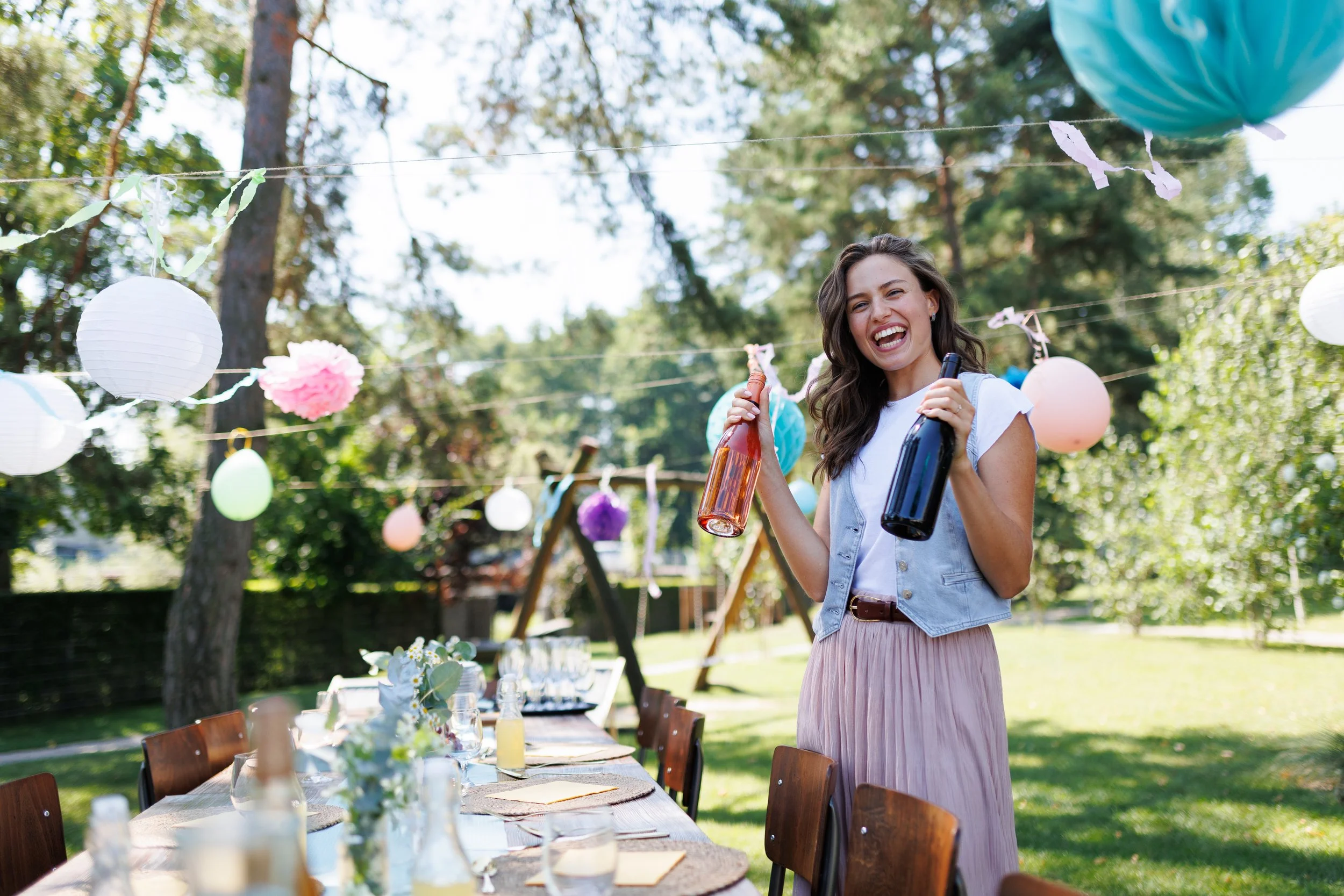 Eine lachende Frau bei einer Gartenparty, die Getränke hält, im Hintergrund bunte Luftballons und Pappteller, die an einer Wäscheleine hängen