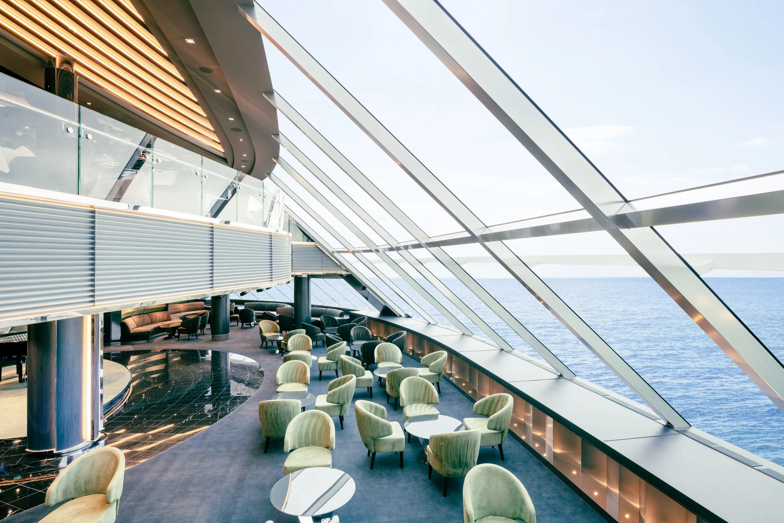 Modern lounge area with green chairs and large windows revealing a view of the ocean.