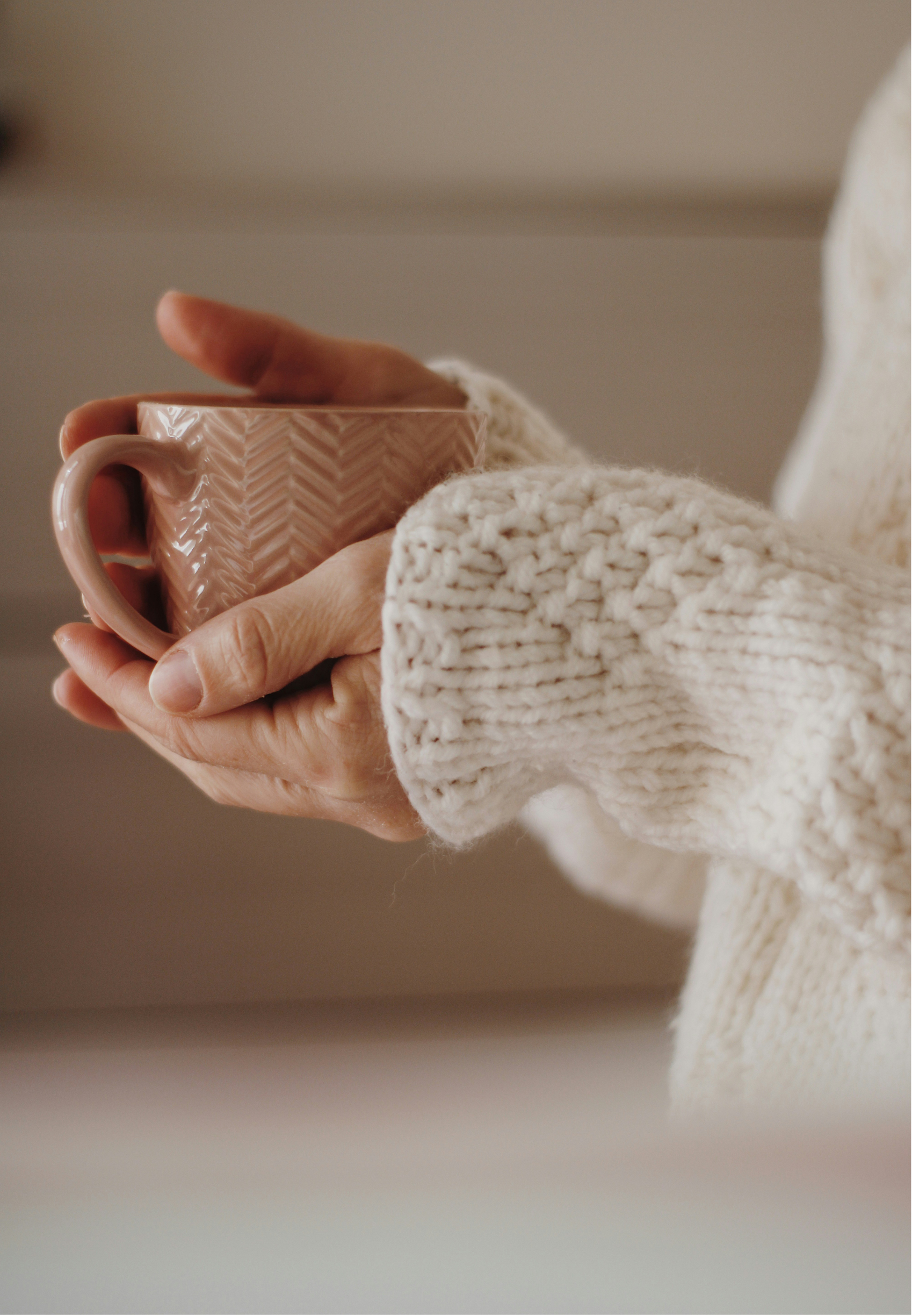 Person holding a pink ceramic mug with a textured zigzag pattern, wearing a chunky white knit sweater.