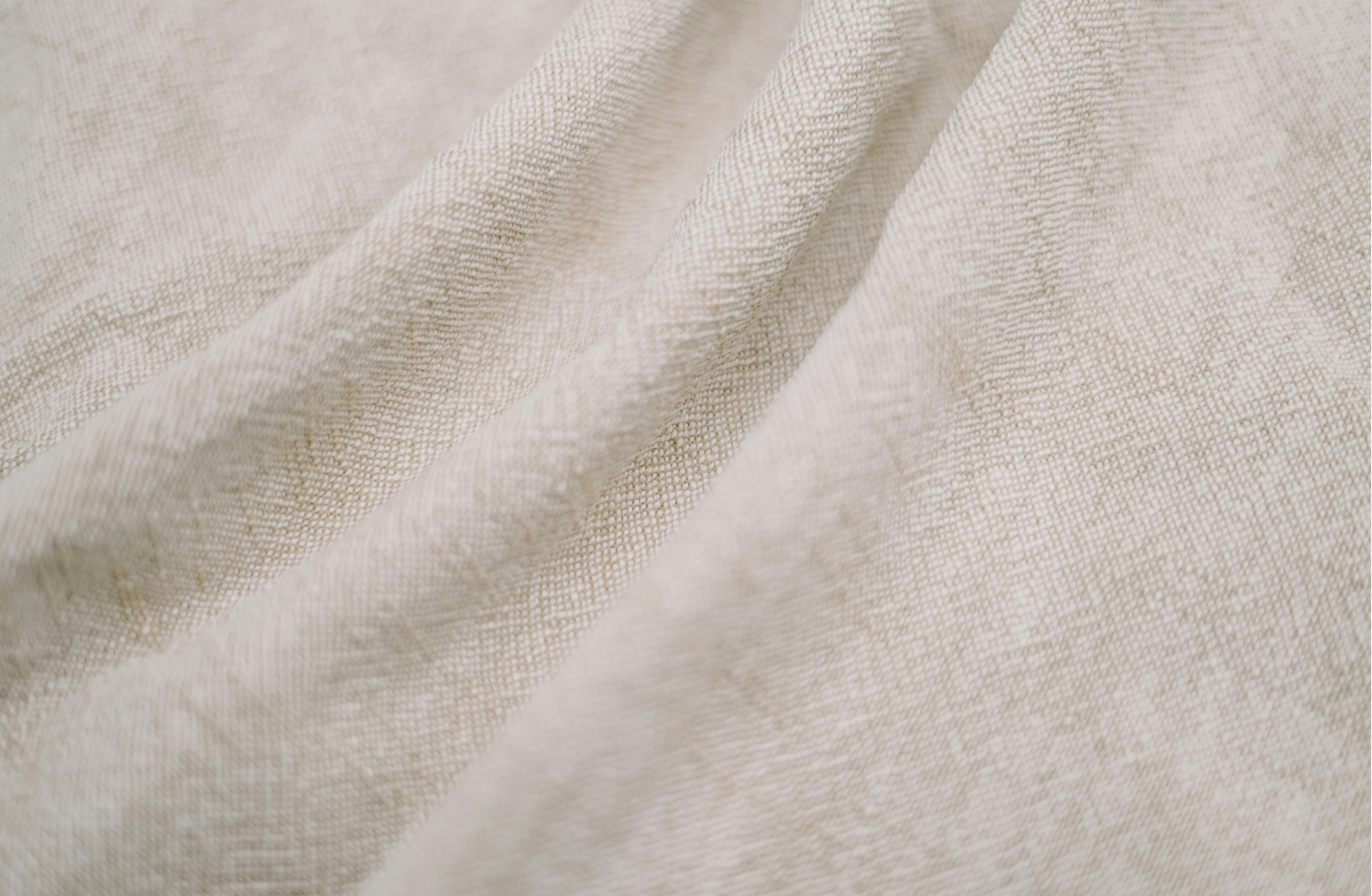 Close-up of beige fabric with a textured weave, showing soft folds and natural appearance.