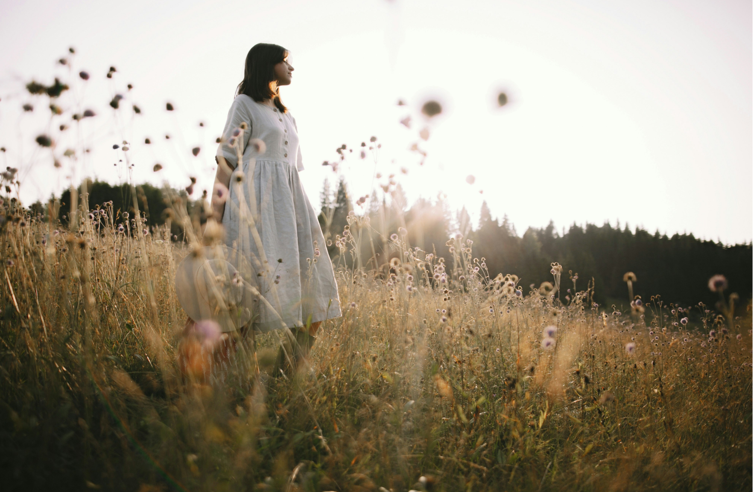 A woman standing in a field of flowers during sunset or sunrise.