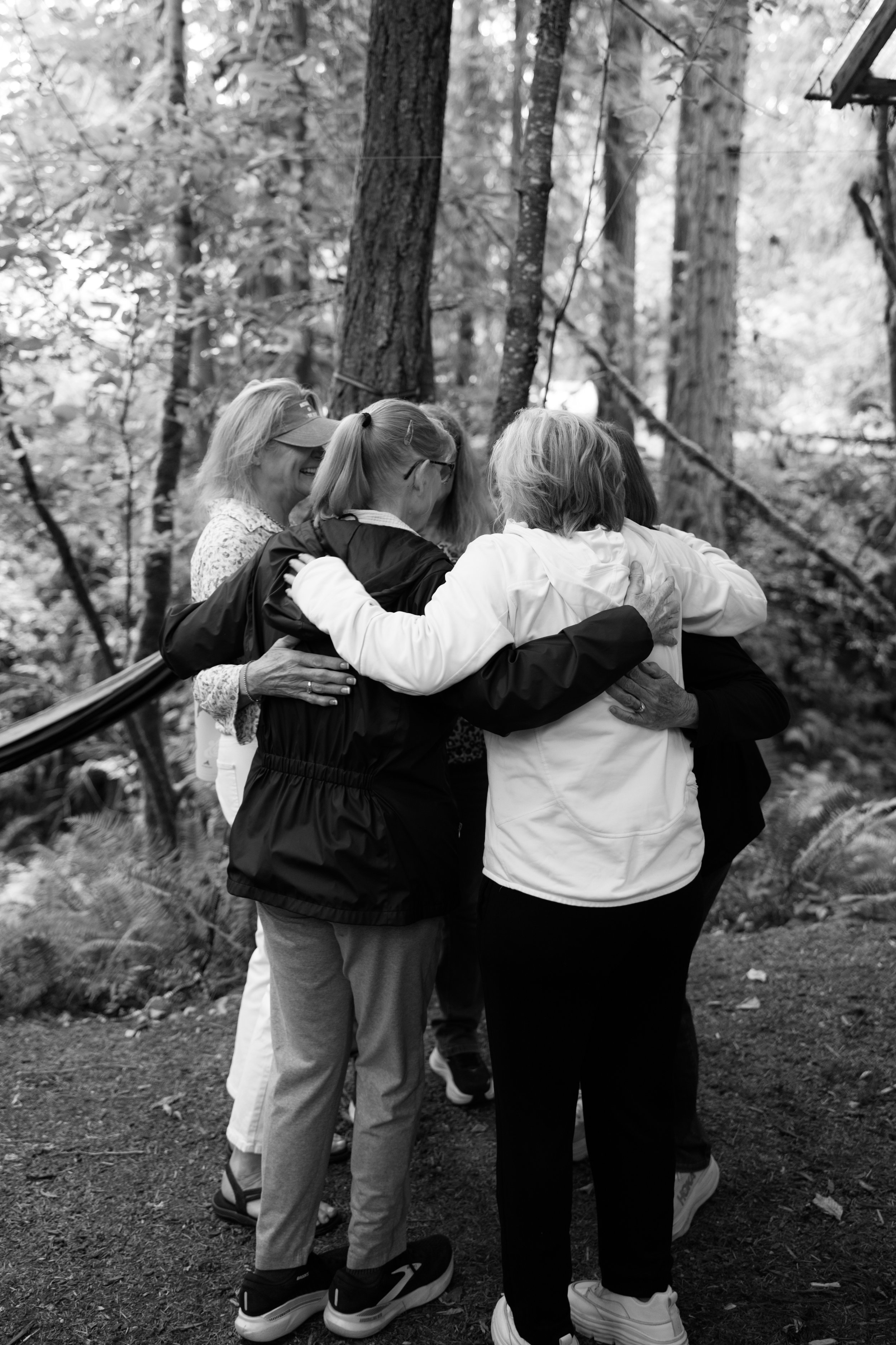 A group of people hugging in a circle outdoors in a forest setting.