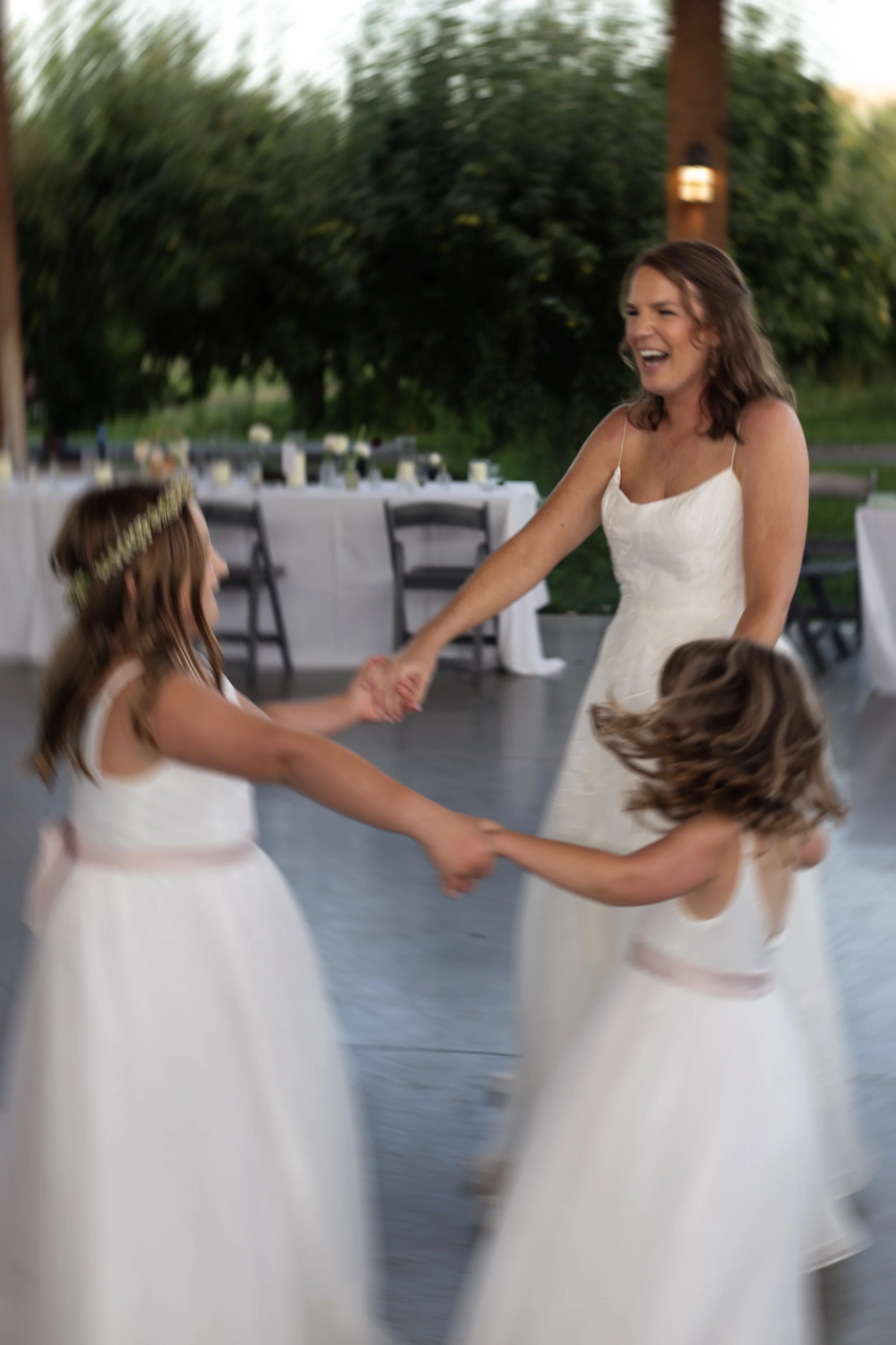 Women and girls dancing and holding hands at an outdoor wedding reception.