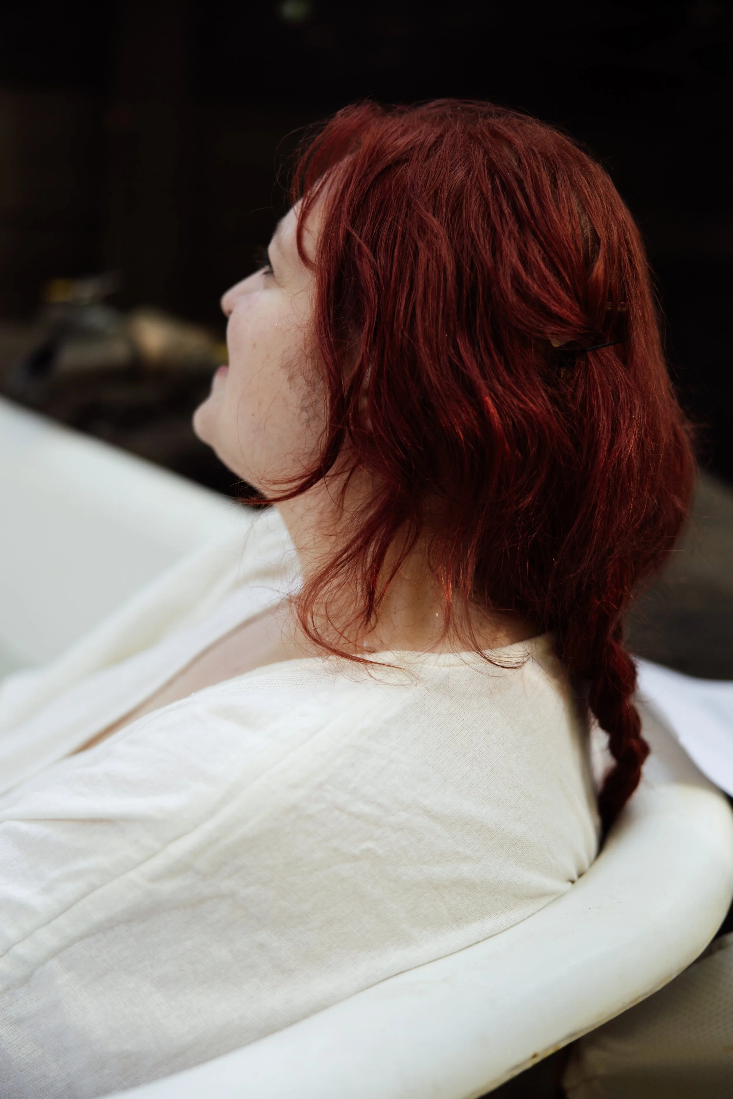 Close-up side profile of a woman with red, wavy hair wearing a white top.