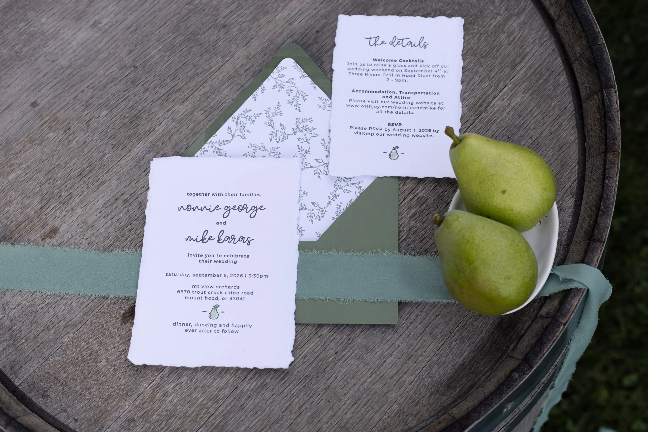 Wedding invitation, RSVP card, and a green pear on a wooden table with a bowl of pears.
