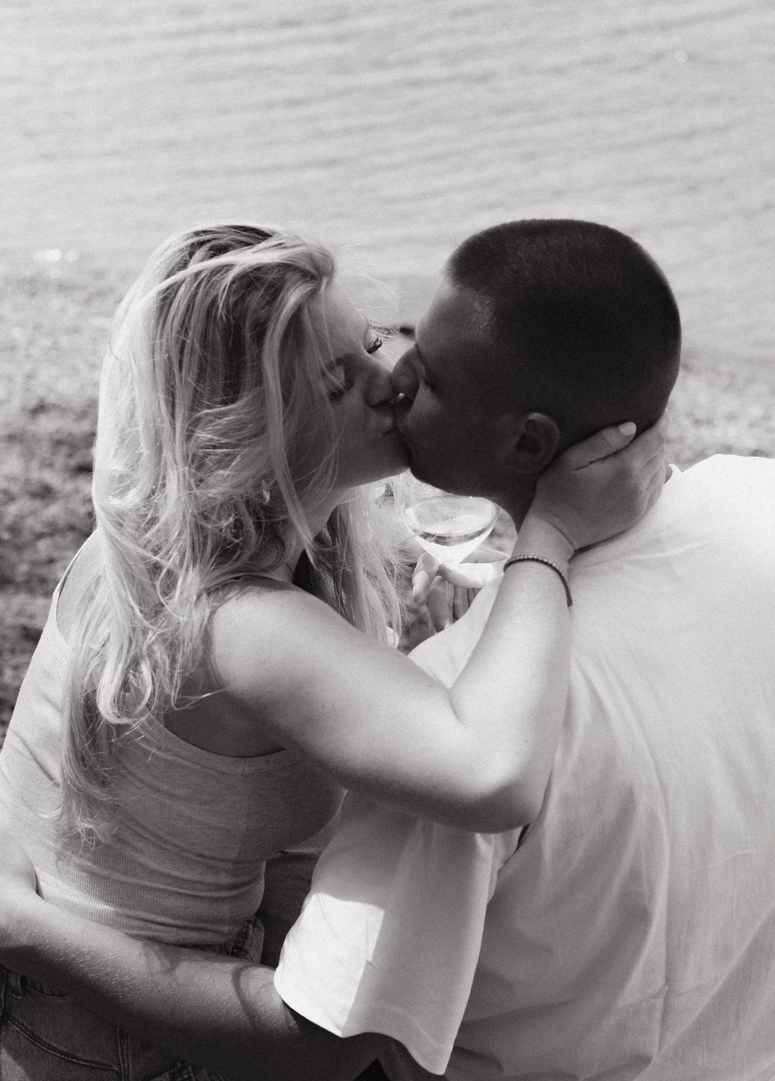 A black and white photo of a couple kissing on the beach with the ocean in the background.