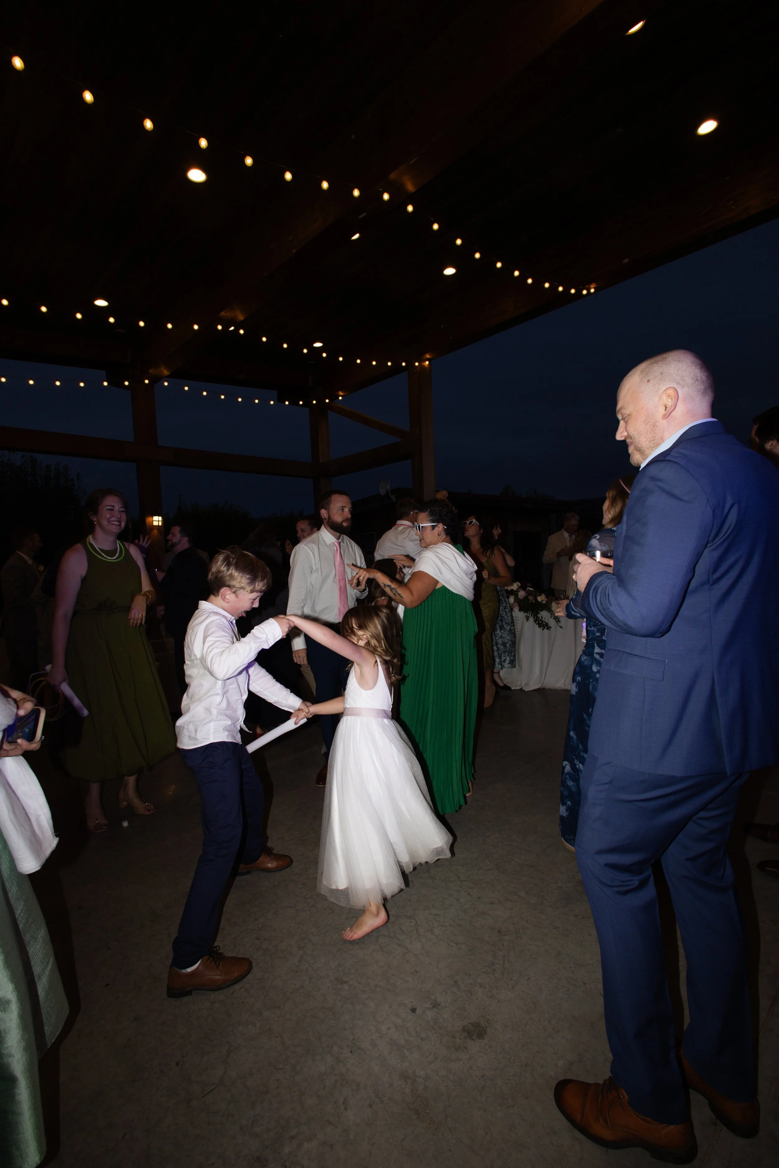 People dancing at a wedding reception under string lights on a covered outdoor patio at night.