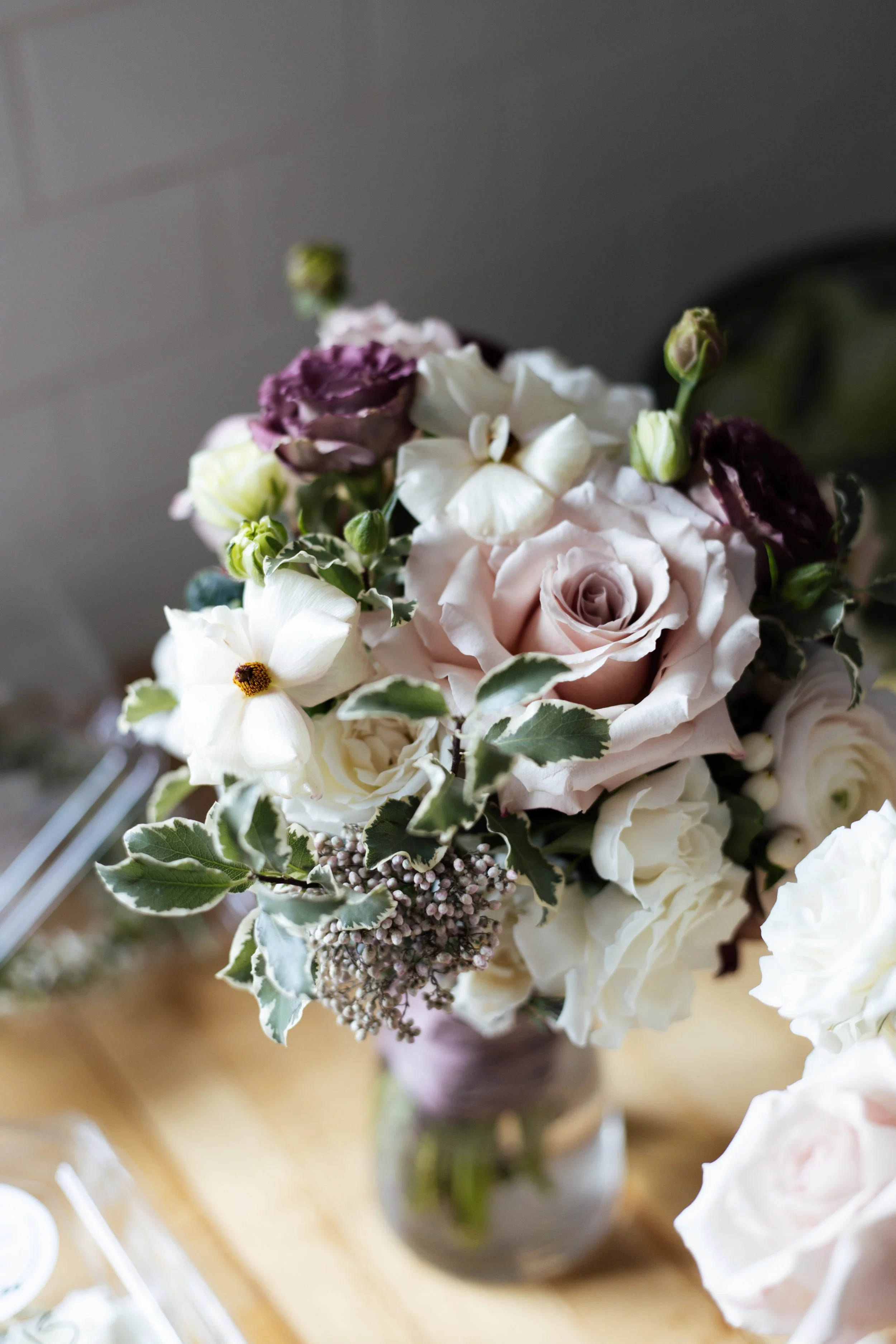 Close-up of a bouquet of mixed flowers in a glass vase with white, pink, purple, and green flowers and leaves.