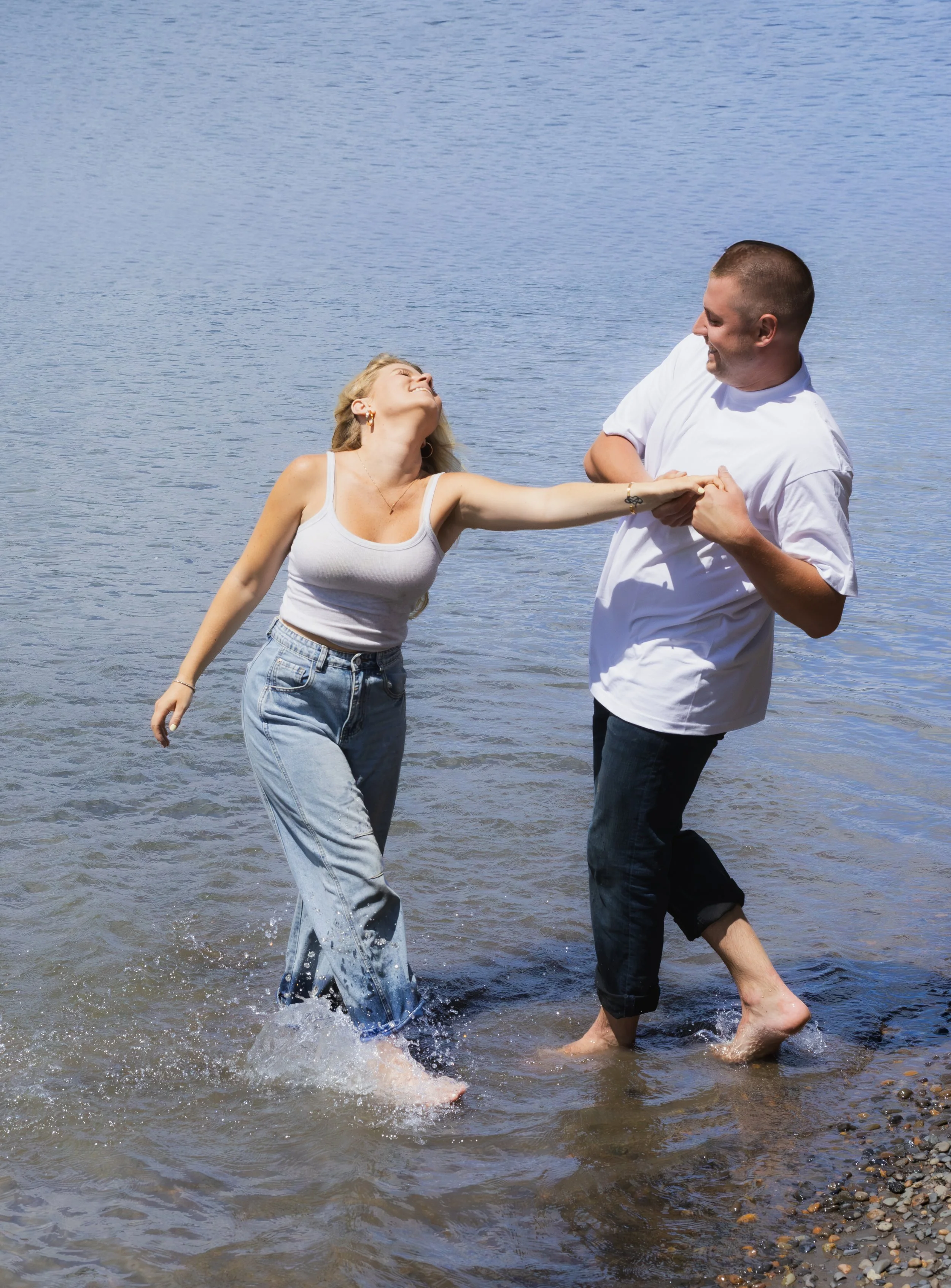 A woman and a man are holding hands and dancing in shallow water at the beach, smiling and enjoying each other's company.