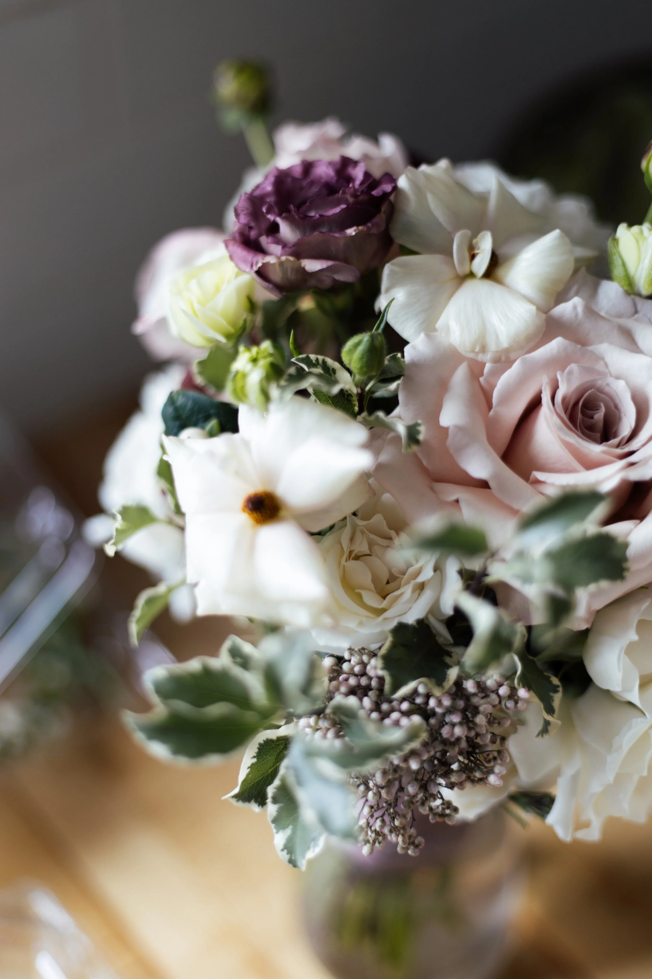 Close-up of a bouquet of flowers including white roses, purple lisianthus, and white daisies, with green leaves and buds.