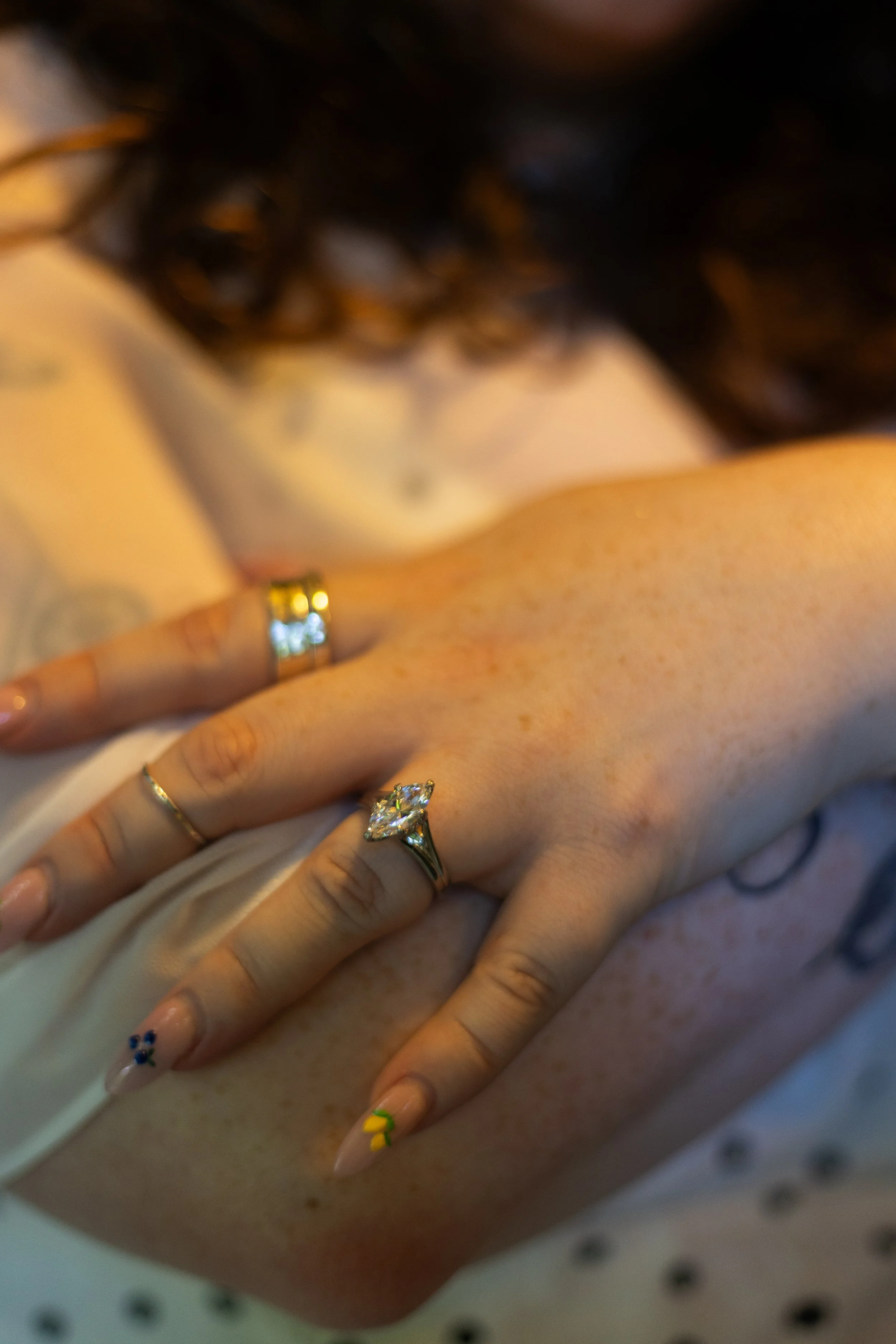 Close-up of a person's hand with multiple rings and decorated nails, resting on a skin surface, possibly a person's chest.