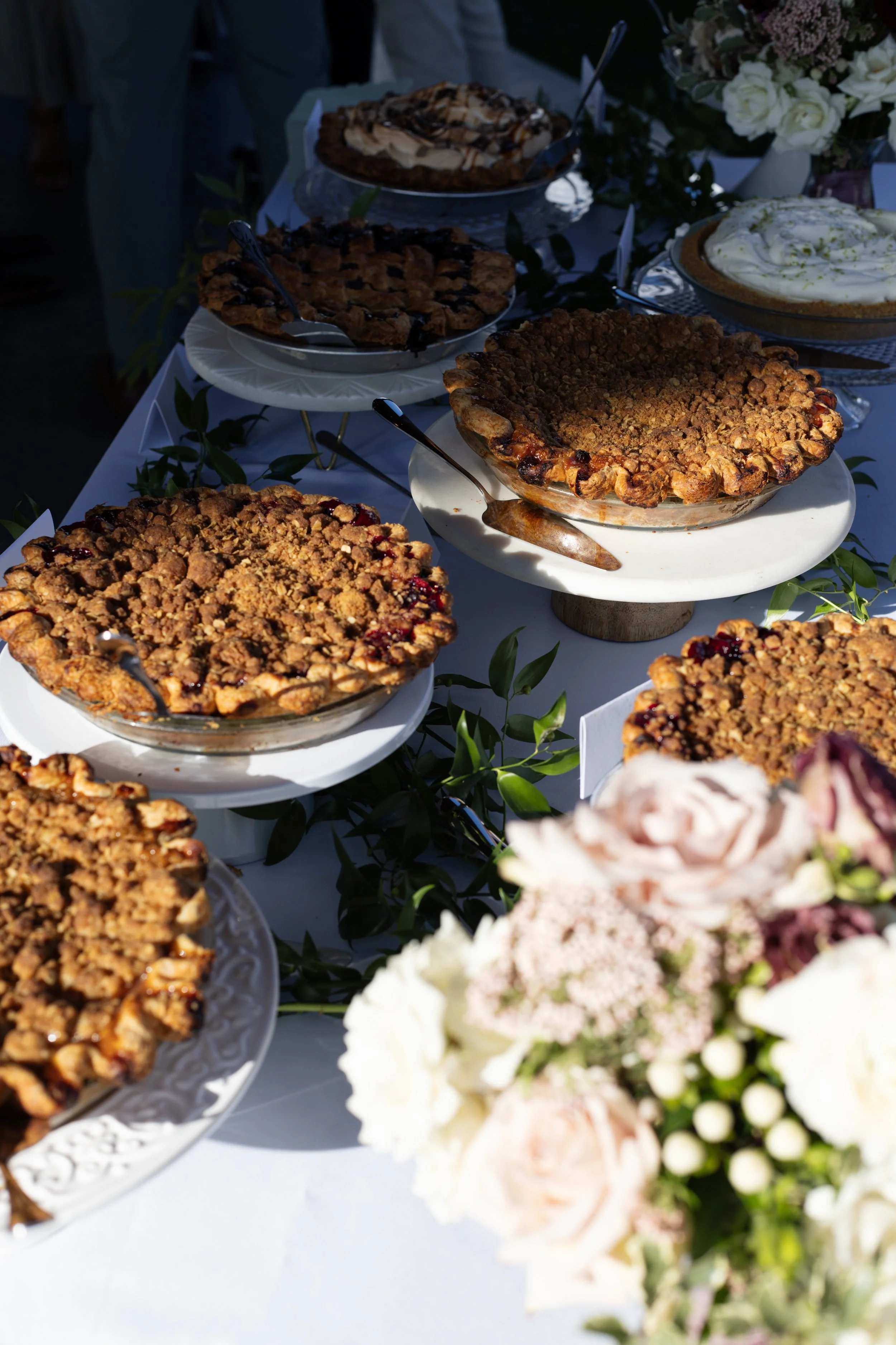A display of assorted pies on a table, with a bouquet of flowers in the foreground.