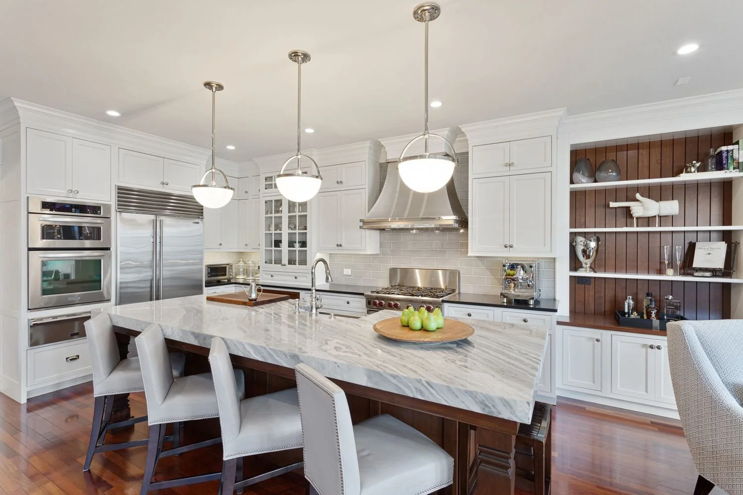 White kitchen with a marble island, counter stools and three pendant lights