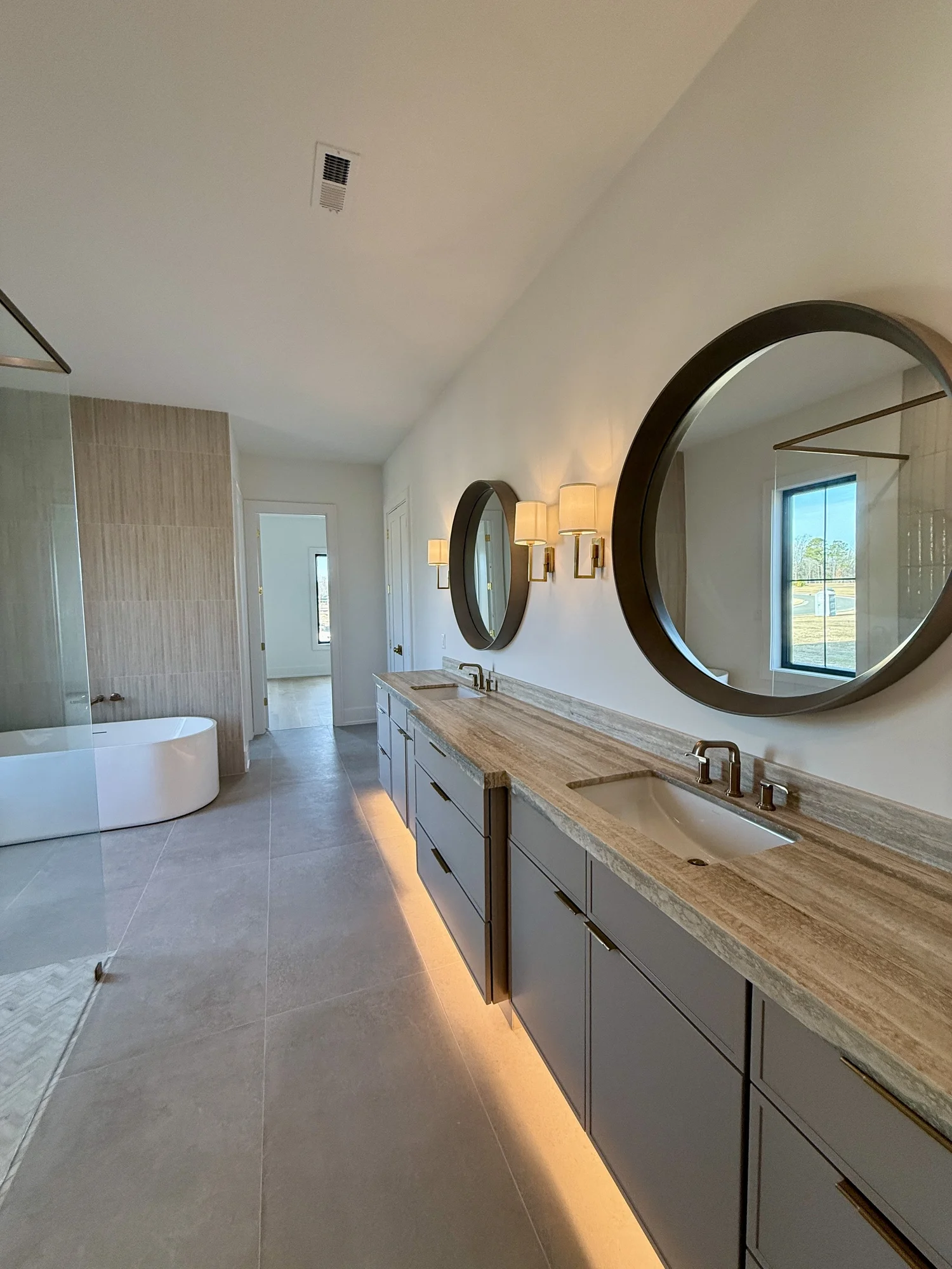 Primary bath double vanity with round mirrors, wall sconces and a freestanding tub