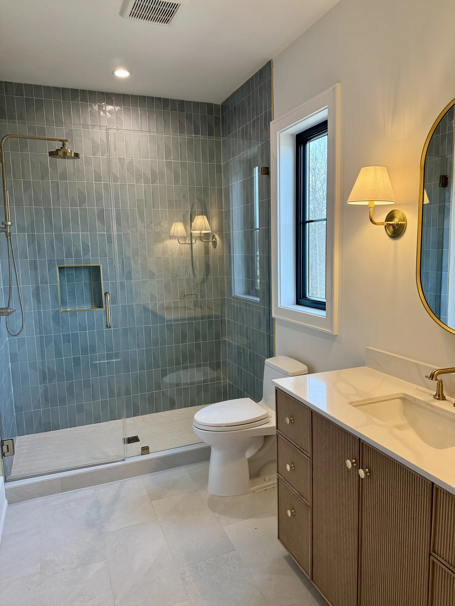 Guest bath with blue-green tile shower, round mirror and brass sconces