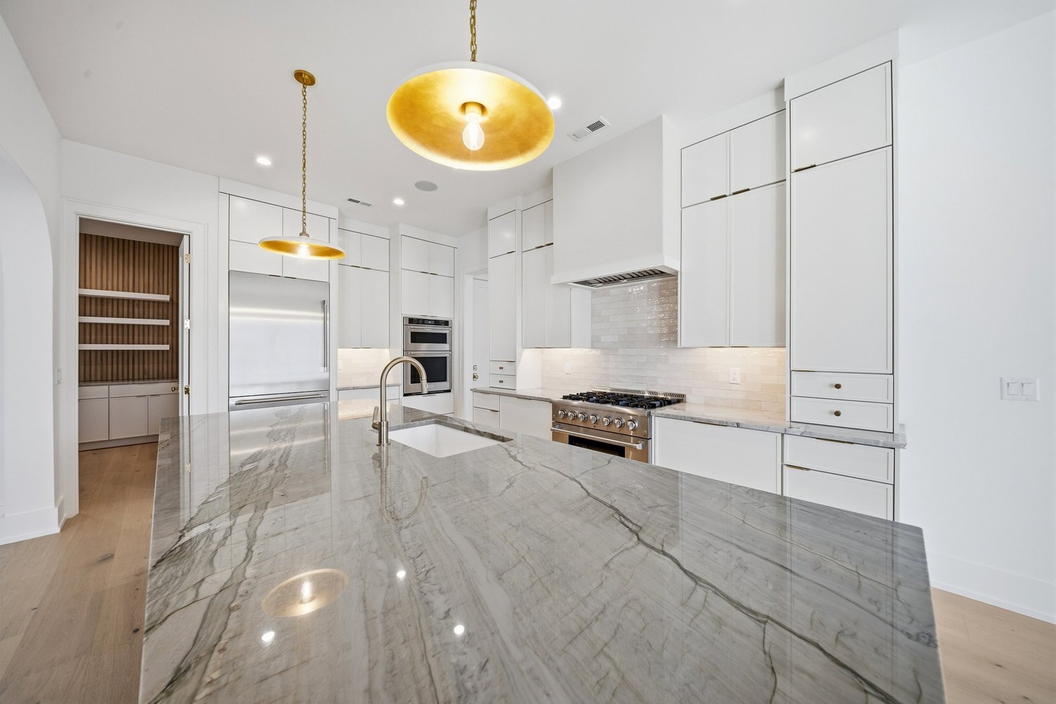 Stone-topped kitchen island with brass pendants and a professional-style range