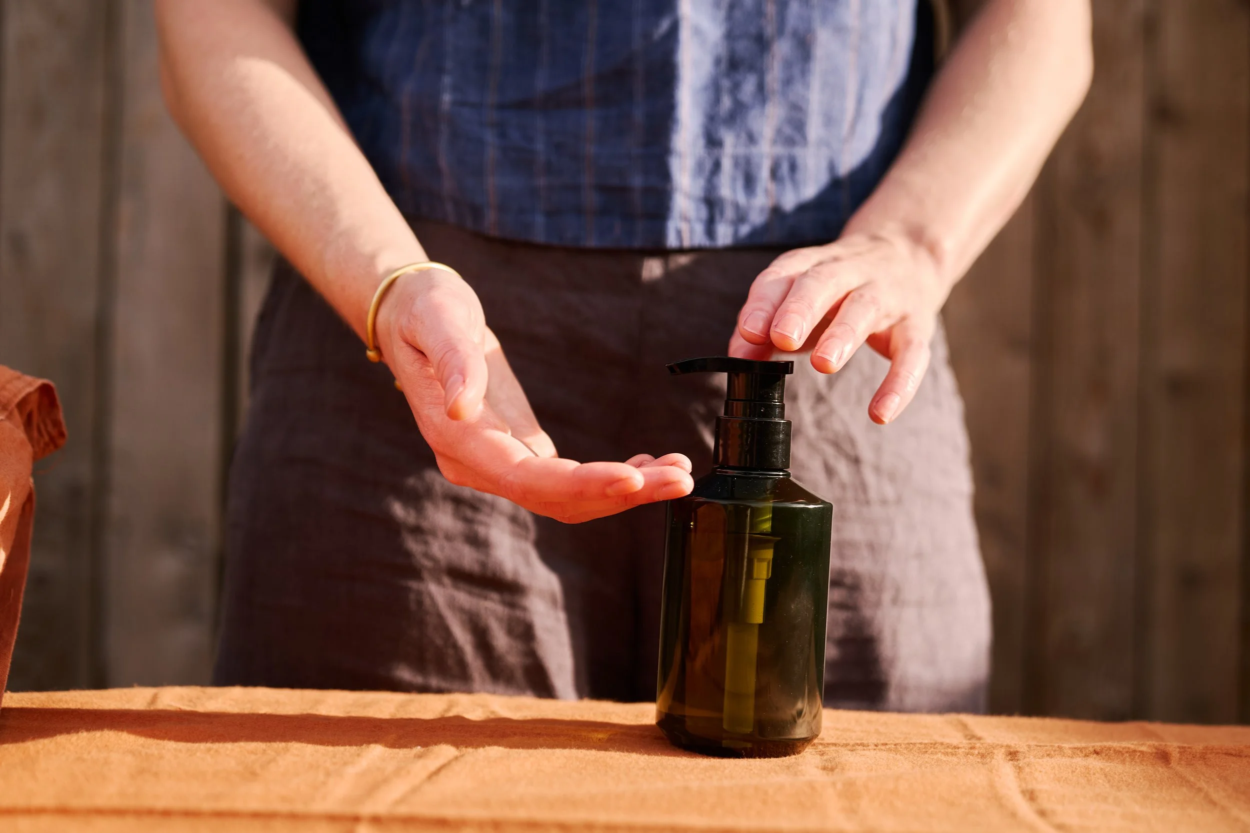 Person pressing a pump dispenser on a dark green-coloured bottle of oil on a massage table.