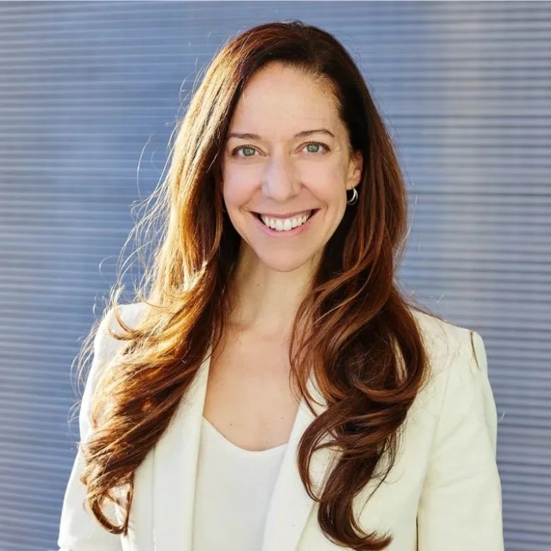 Monica Arés smiling in a cream-colored blazer in front of a gray background