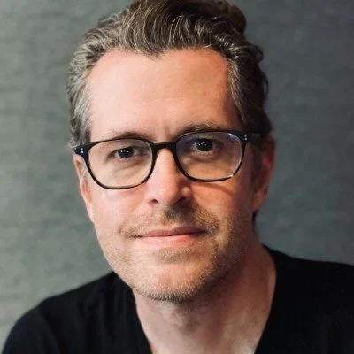 Brad MacDonald in glasses and a black shirt against a gray background