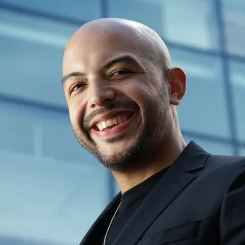 Dr. Danny Pimentel smiling outdoors in front of a modern glass building