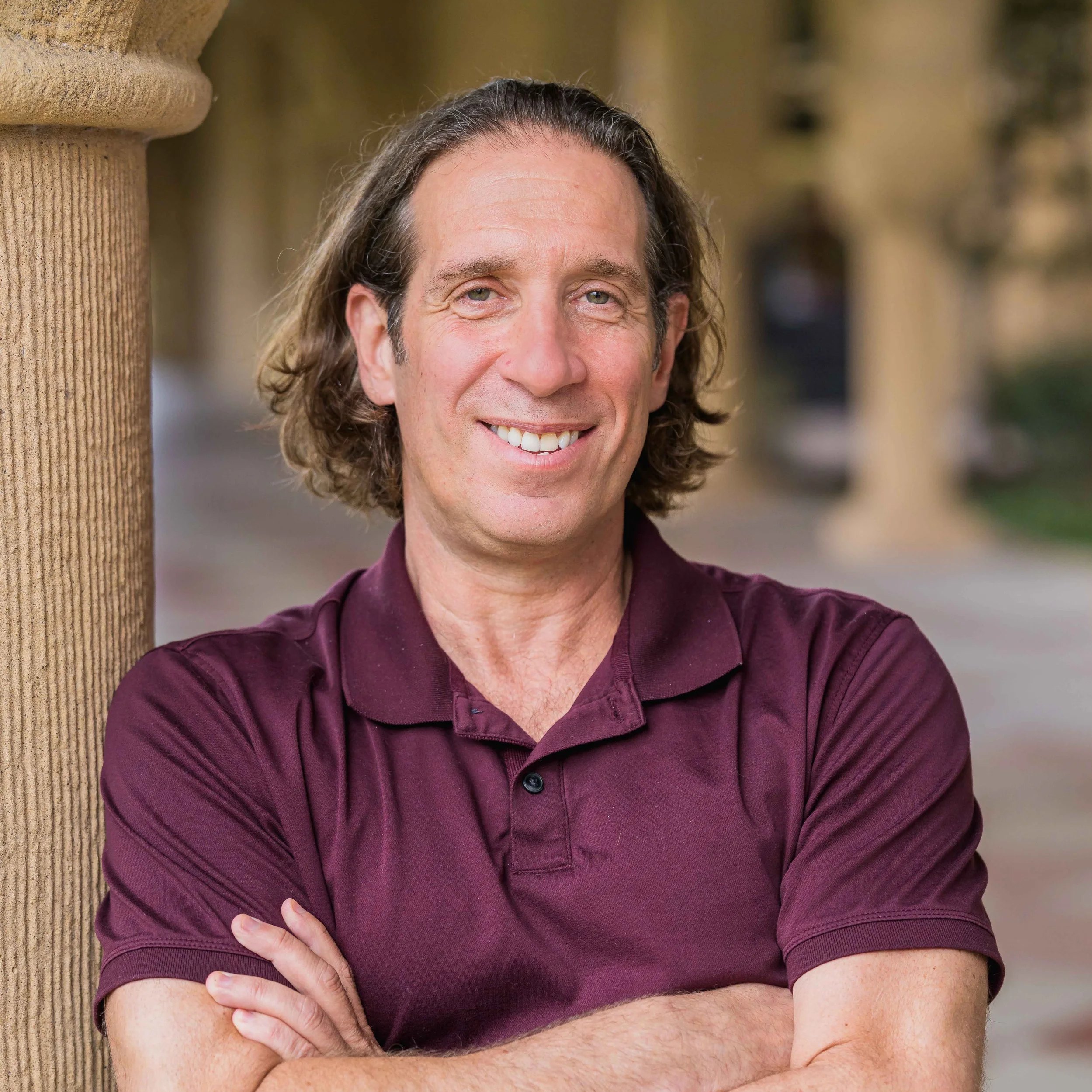 Prof. Jeremy Bailenson smiling while leaning against a stone pillar outdoors