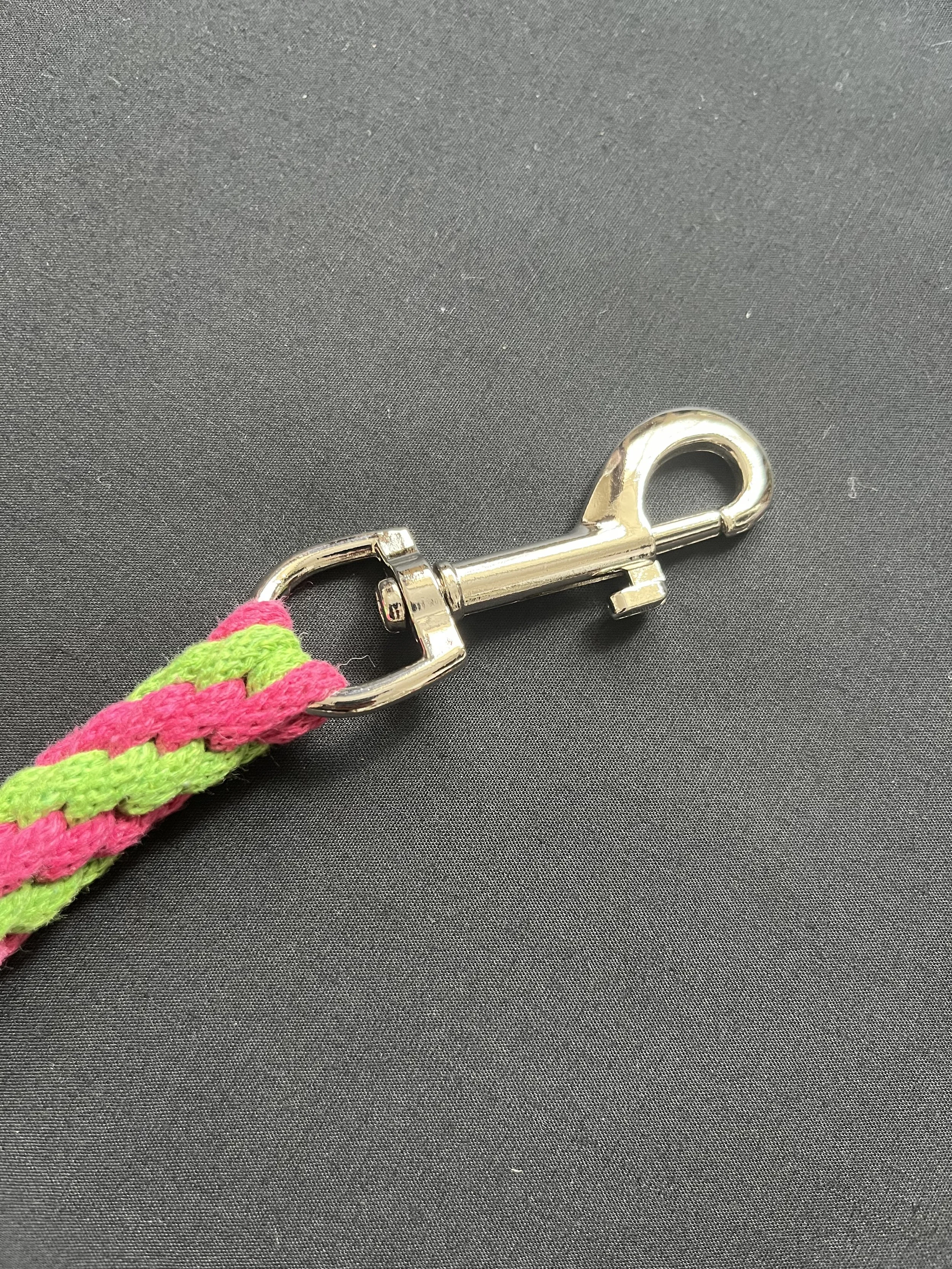 Close-up of a metal clasp attached to a colorful pink and green braided strap on black background.