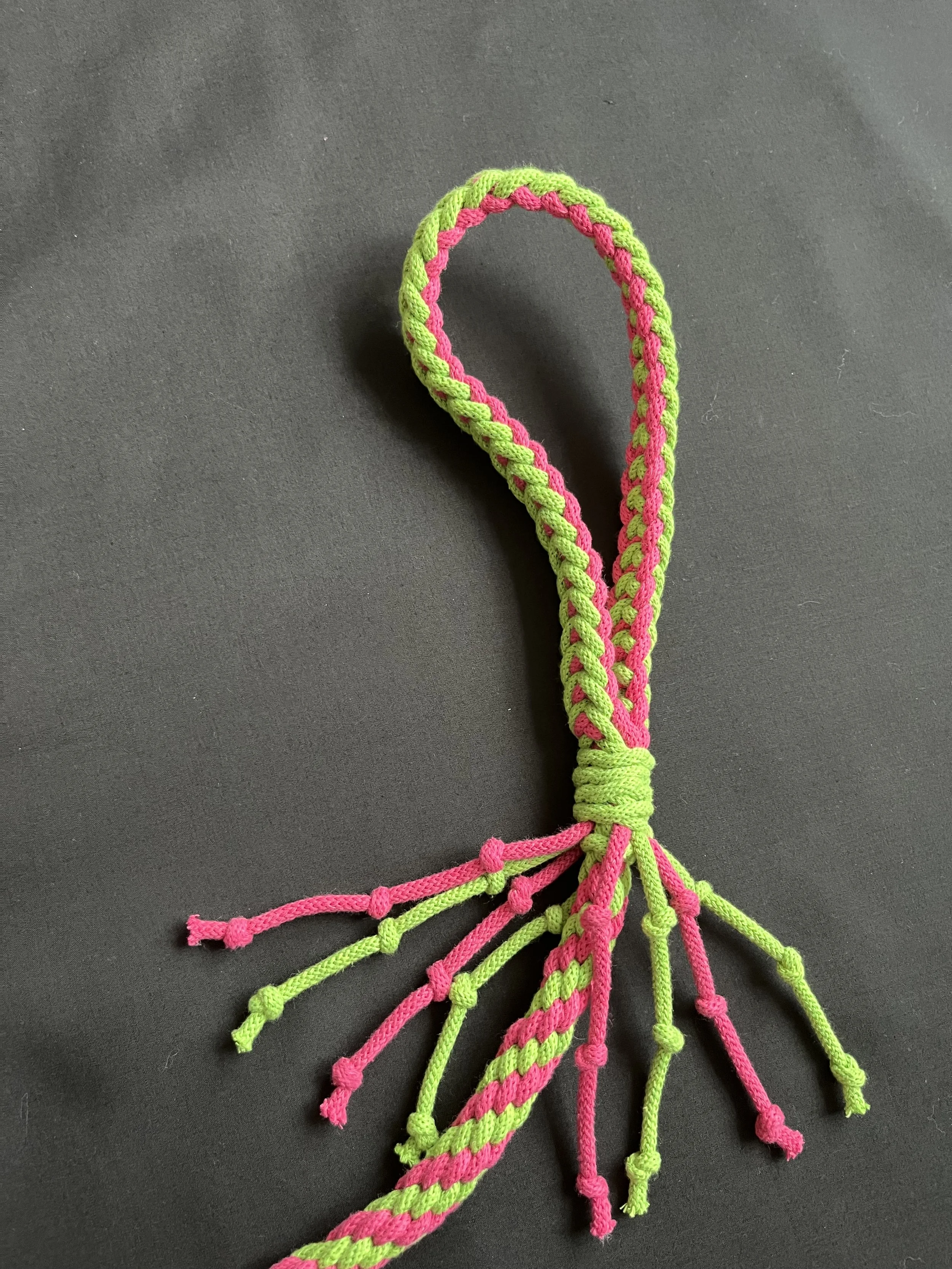 Colorful braided friendship bracelet with pink and green threads on a black surface.