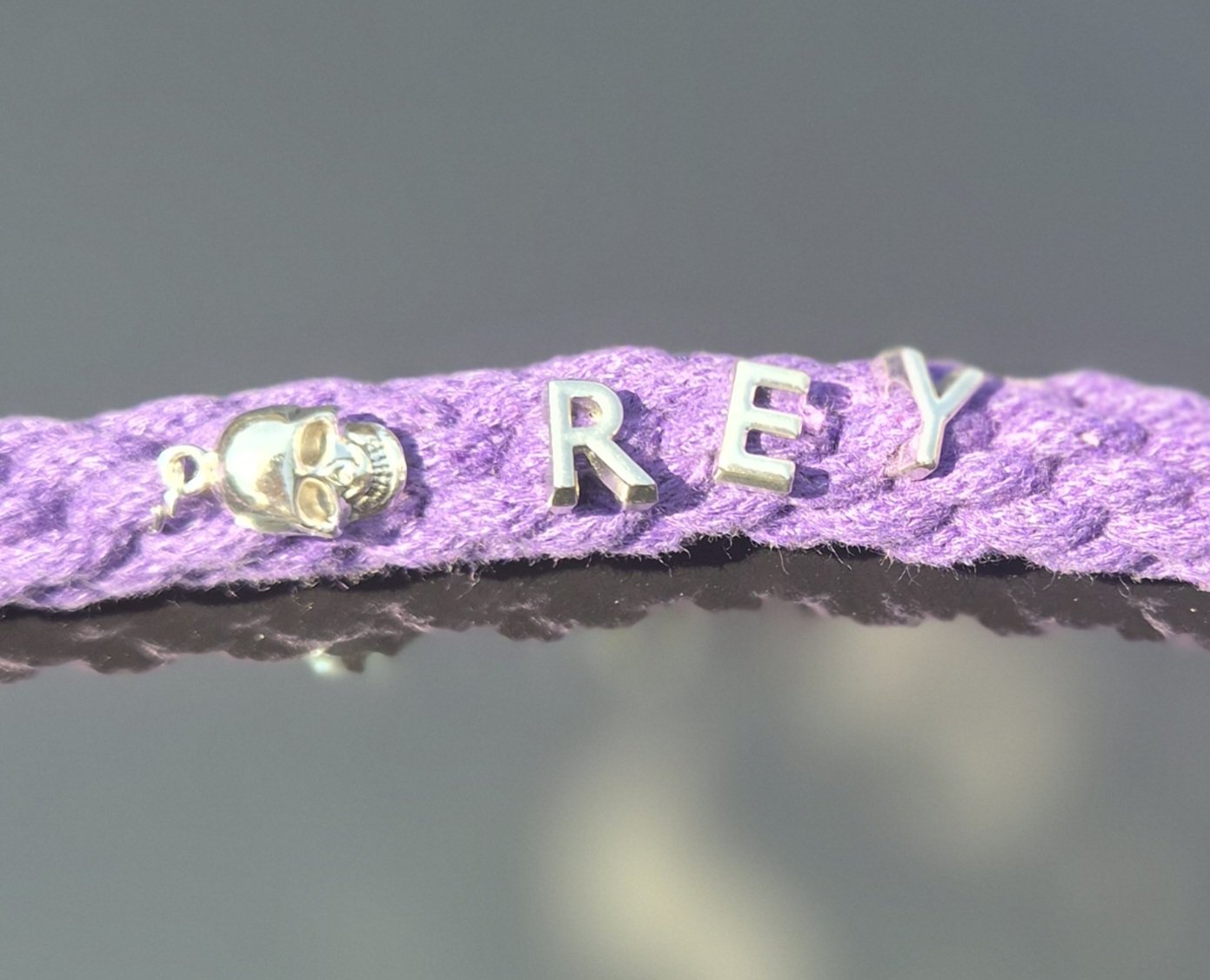 A purple dog lead with silver-tone metal letters spelling 'REY' and a small skull charm on the left side.