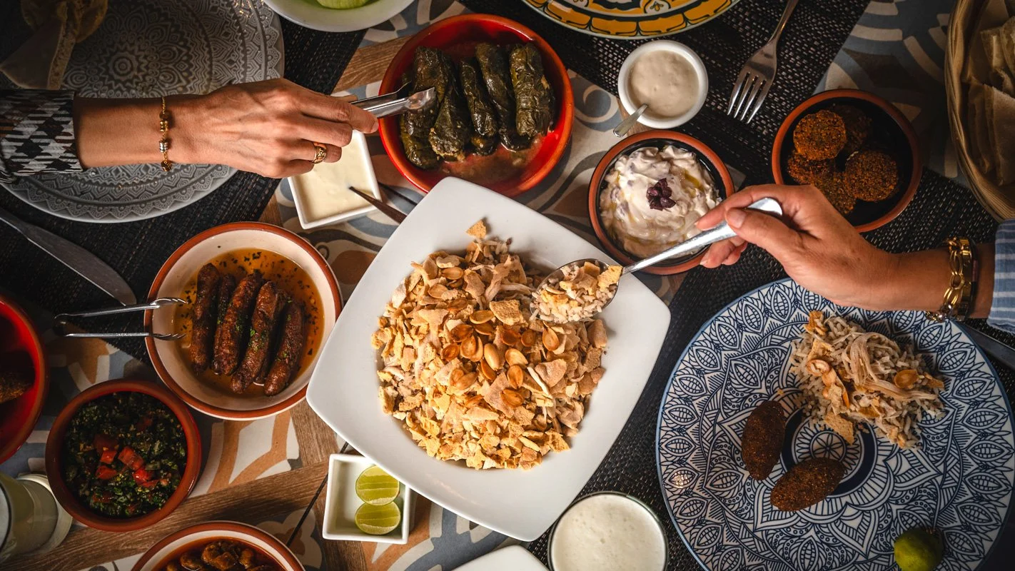 Comida tradicional del Medio Oriente en una mesa, incluyendo hojas de vid rellenas, arroz con pollo, kebabs, ensaladas, yogur, y diversas salsas y acompañamientos.