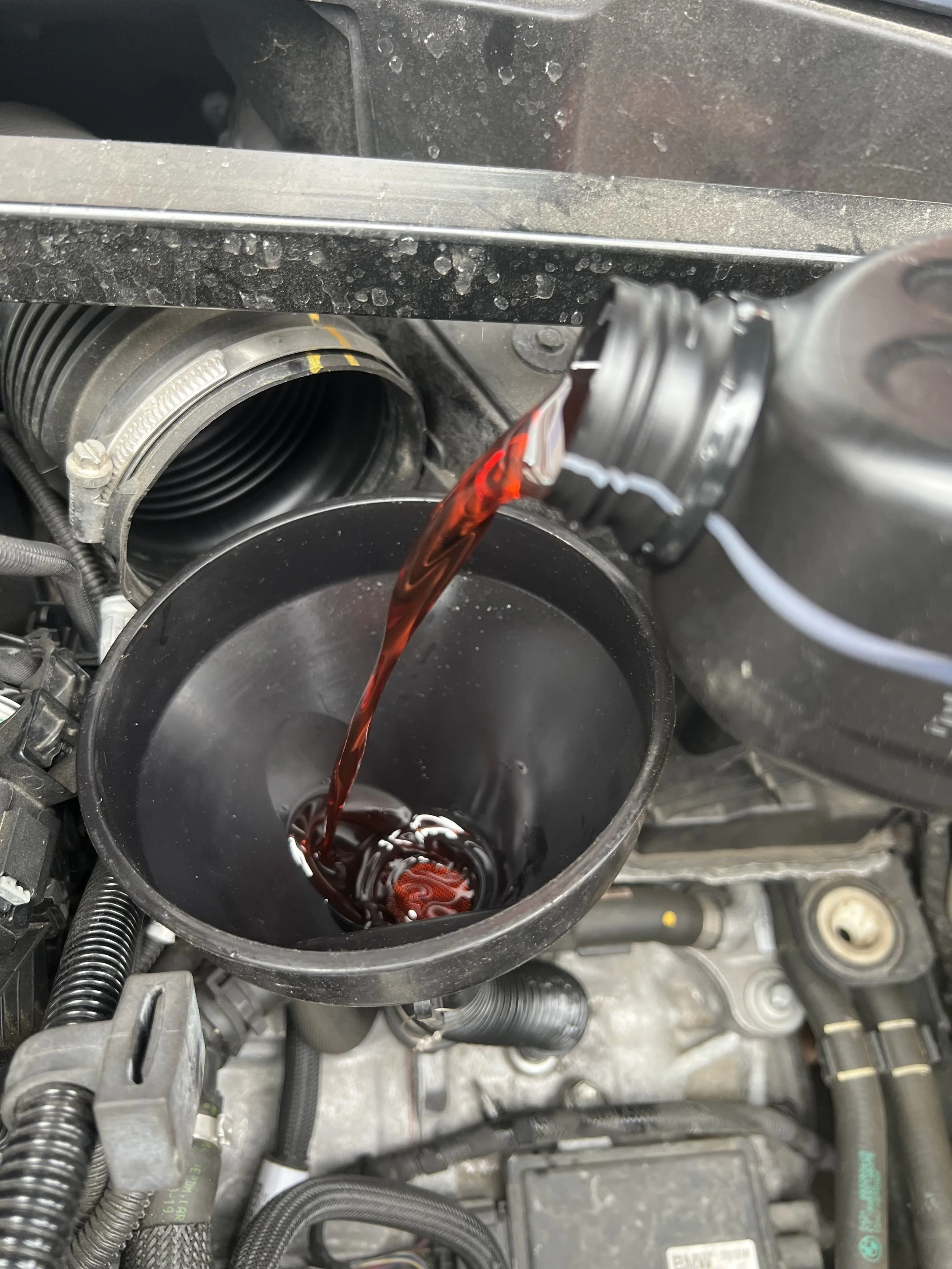 Close-up of a car engine with red-colored oil pouring into a black container.