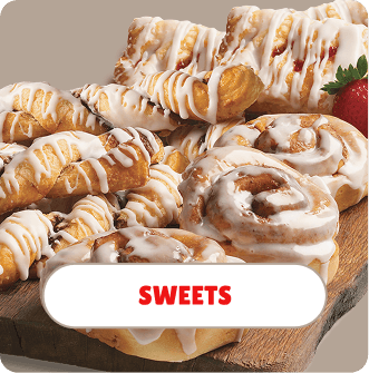 Assorted caramel drizzled pastries and cookies on a wooden tray with a strawberry in the corner.