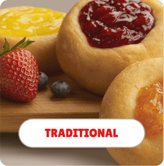 Close-up of traditional doughnuts with fruit topping, including cherry, yellow fruit, and blueberry, on a wooden surface.