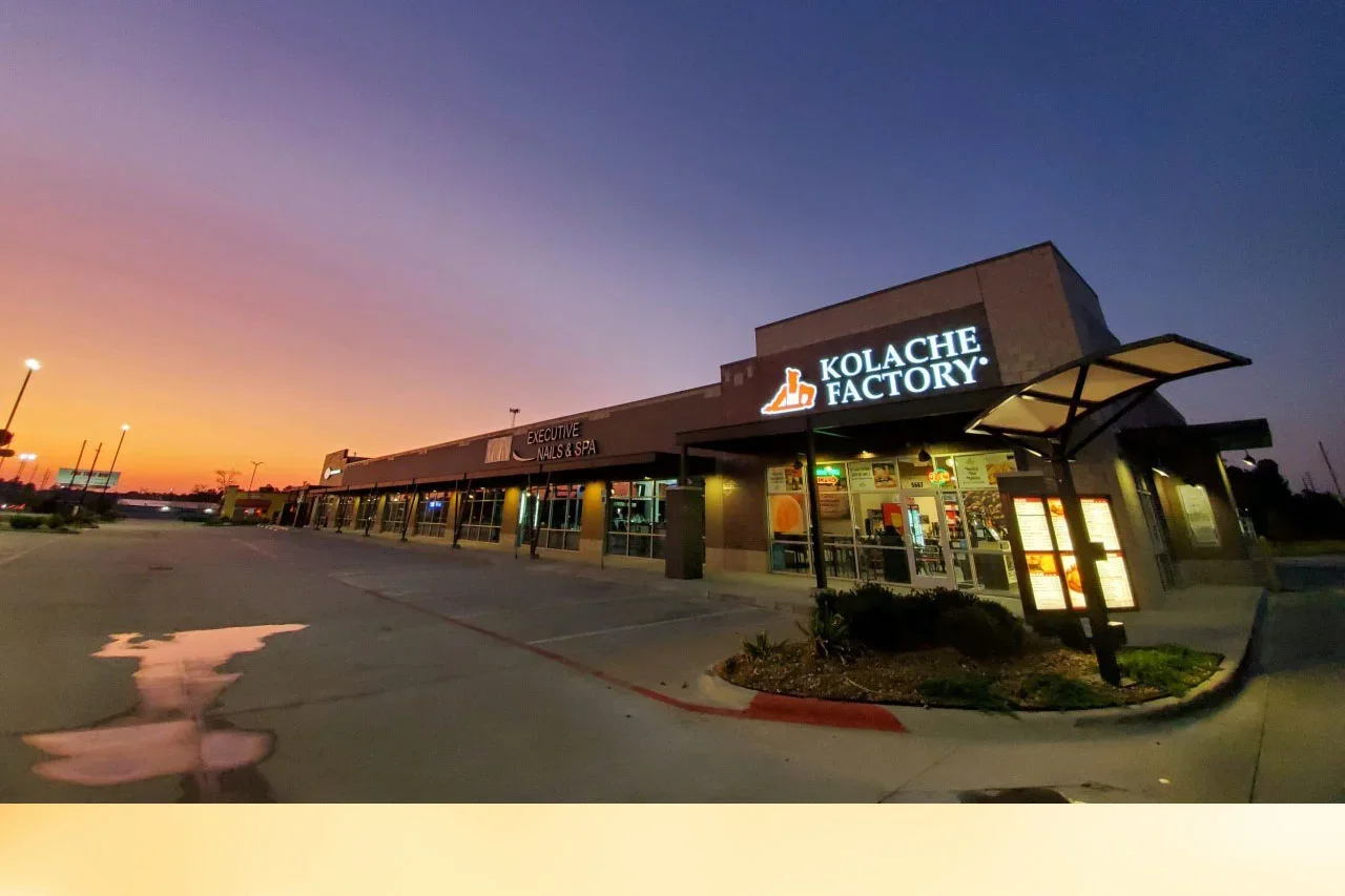 A shopping plaza at sunset with a sign for Kolache Factory.