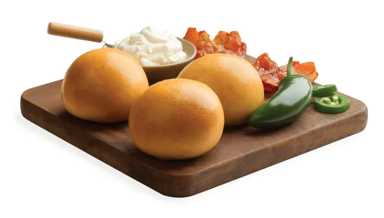 Three kolaches on a wooden cutting board with jalapenos, bacon and cream cheese.