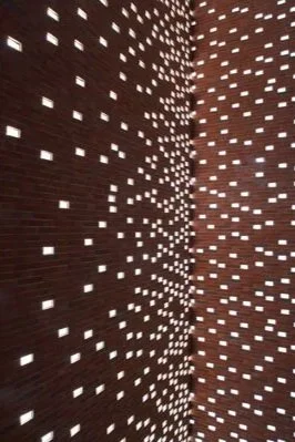 A close-up view of a brick wall with small rectangular cutouts that allow light to pass through, creating a pattern.