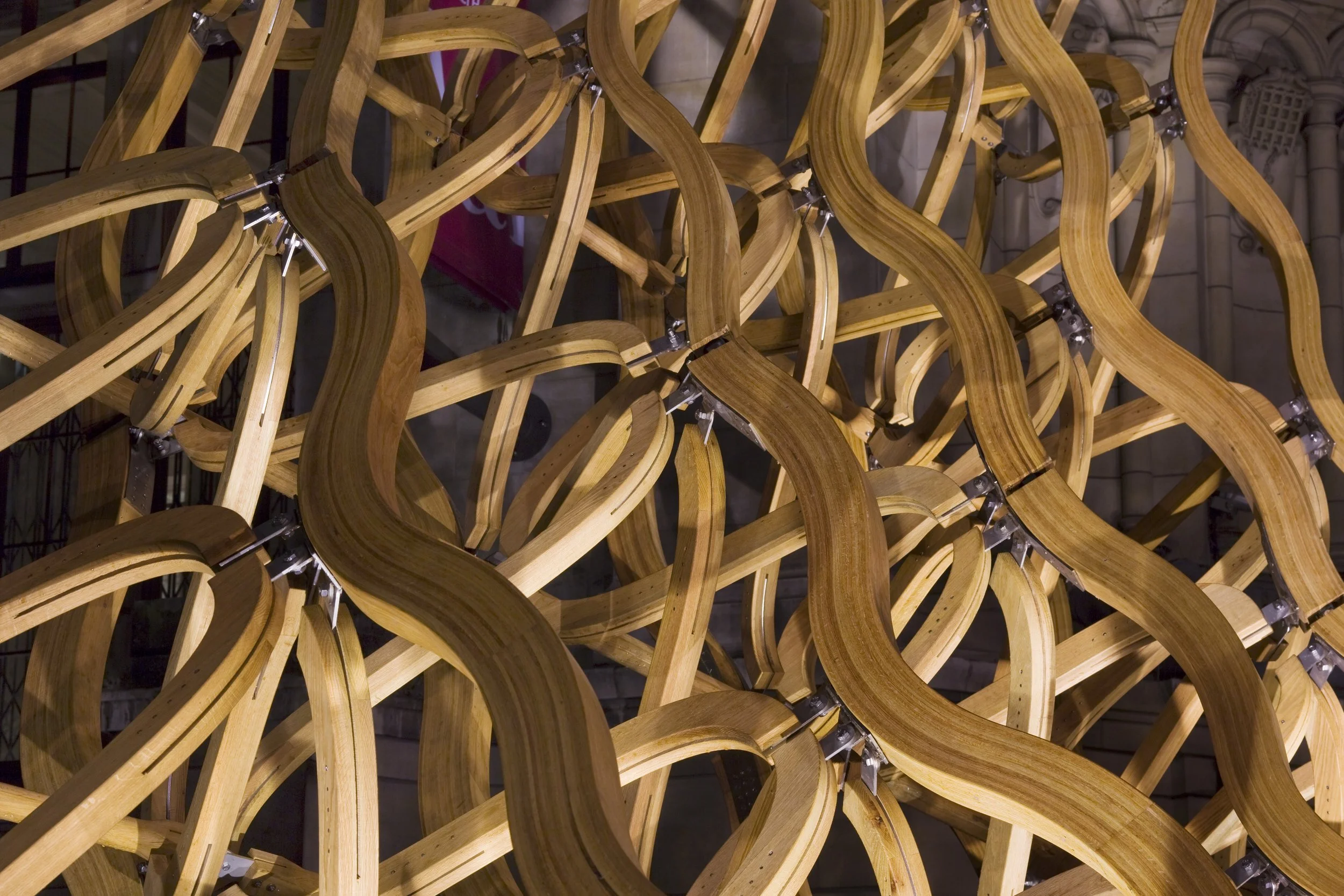 A complex wooden sculpture made of interwoven curved wood strips held together by metal brackets.