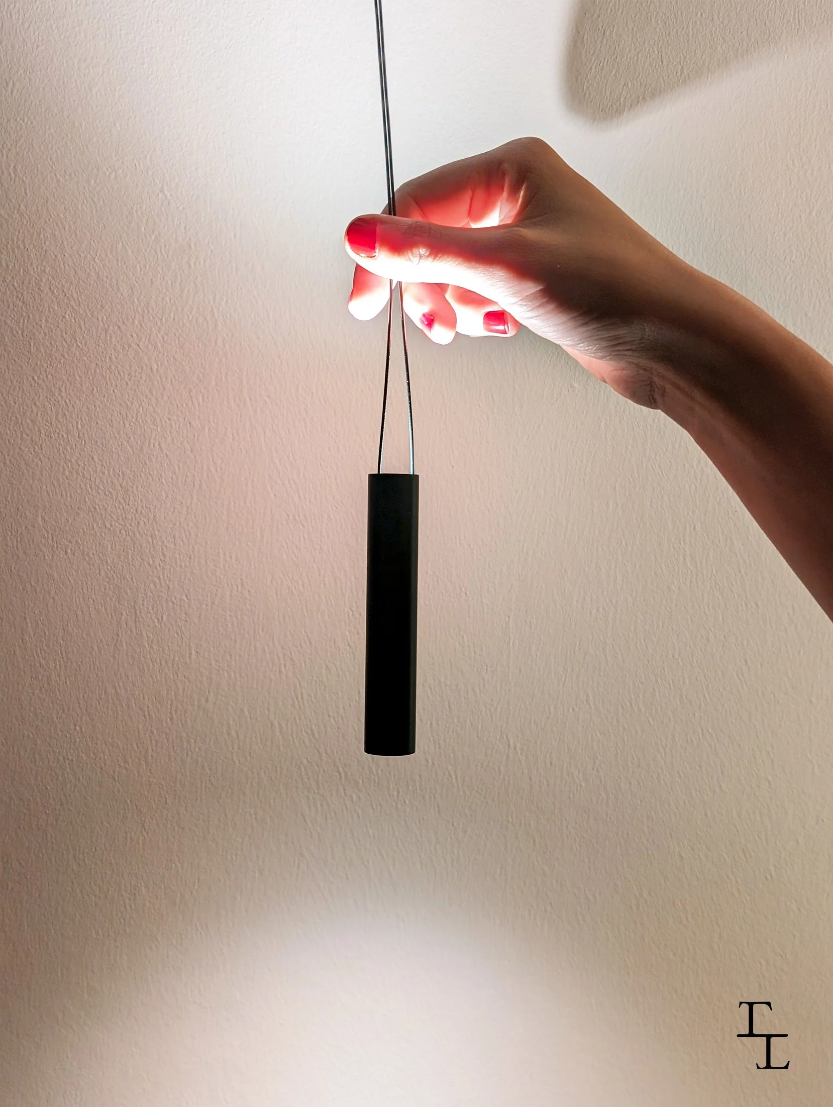 A hand holding a small needle or pin with a black handle, positioned vertically, against a plain wall background.