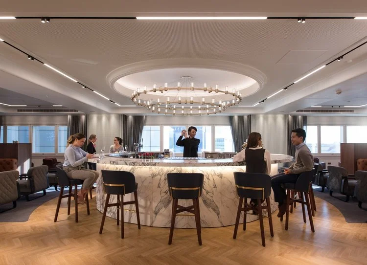 People socializing at a bar in a modern upscale lounge with large windows and elegant decor.