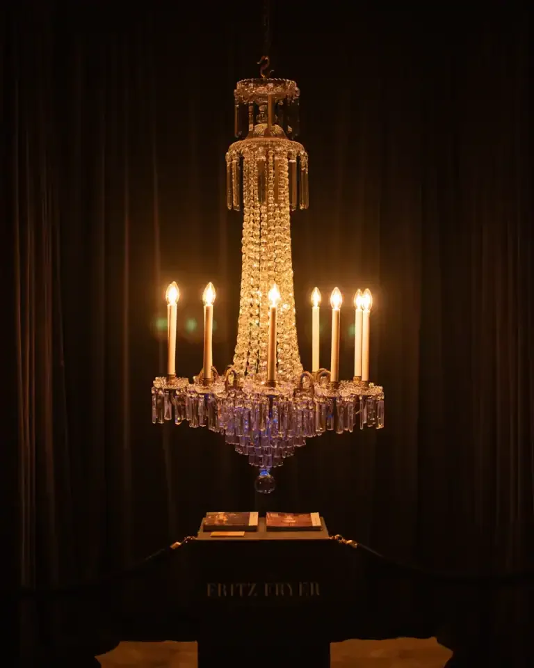 A large, ornate crystal chandelier with multiple candles lit, hanging from the ceiling in a dark room.