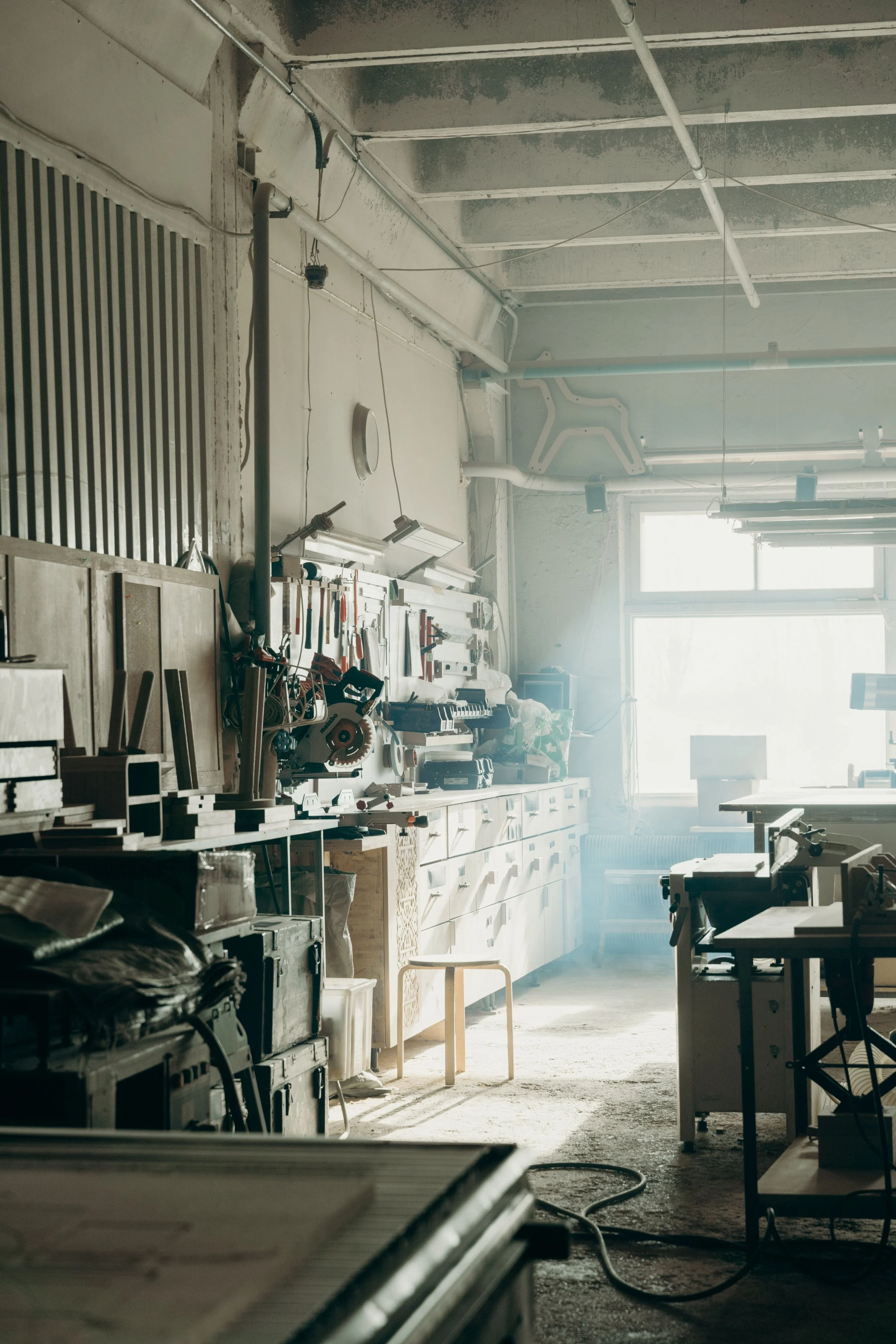A cluttered workshop with tools on the wall, workbenches, and a window letting in natural light.