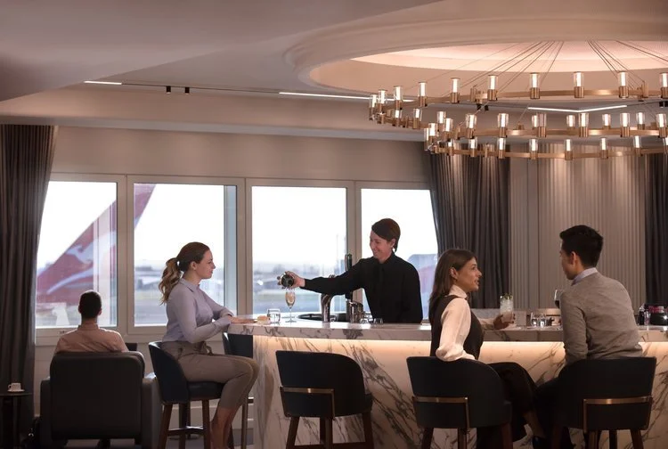 A bartender pouring a drink for a woman sitting at a bar in an upscale lounge with large windows and modern decor.