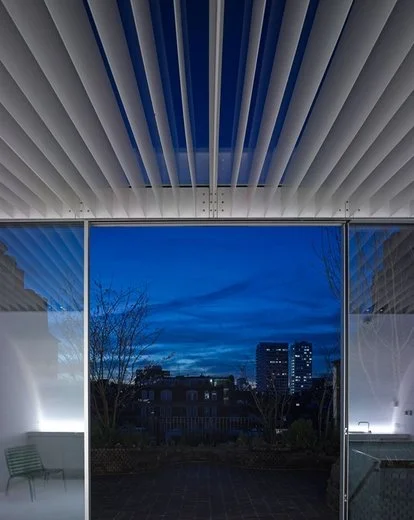 View of a city skyline at dusk through floor-to-ceiling window with a modern ceiling design.