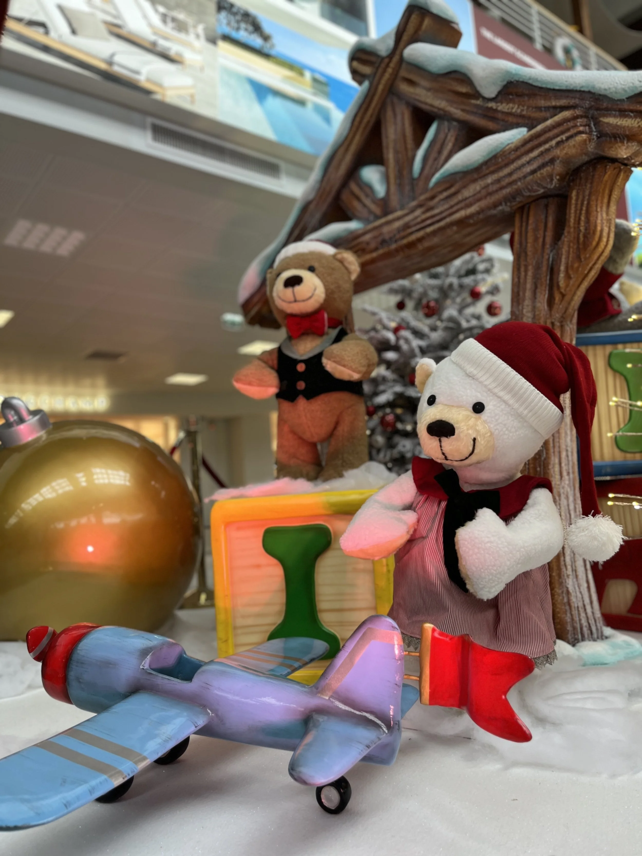 Décoration de Noël mettant en scène des peluches ours en peluche déguisées en Père Noël et en lutin, des luges en bois ornées de motifs hivernaux et des décorations de Noël dans un décor de magasin.