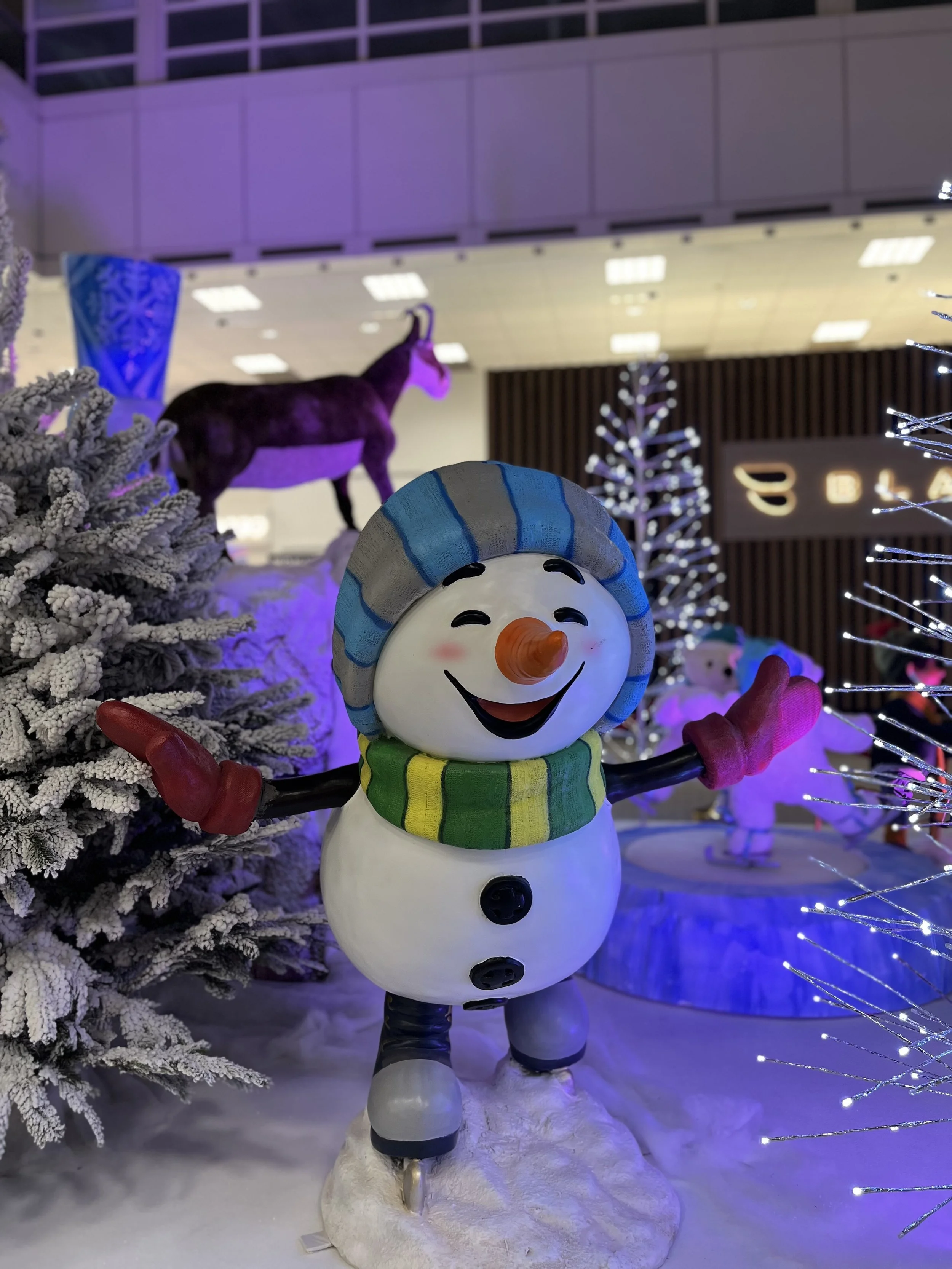 Décoration de Noël dans un aéroport, avec des décorations festives, des automates animatroniques en peluche et des illuminations de Noël. et un bonhomme de neige en résine.