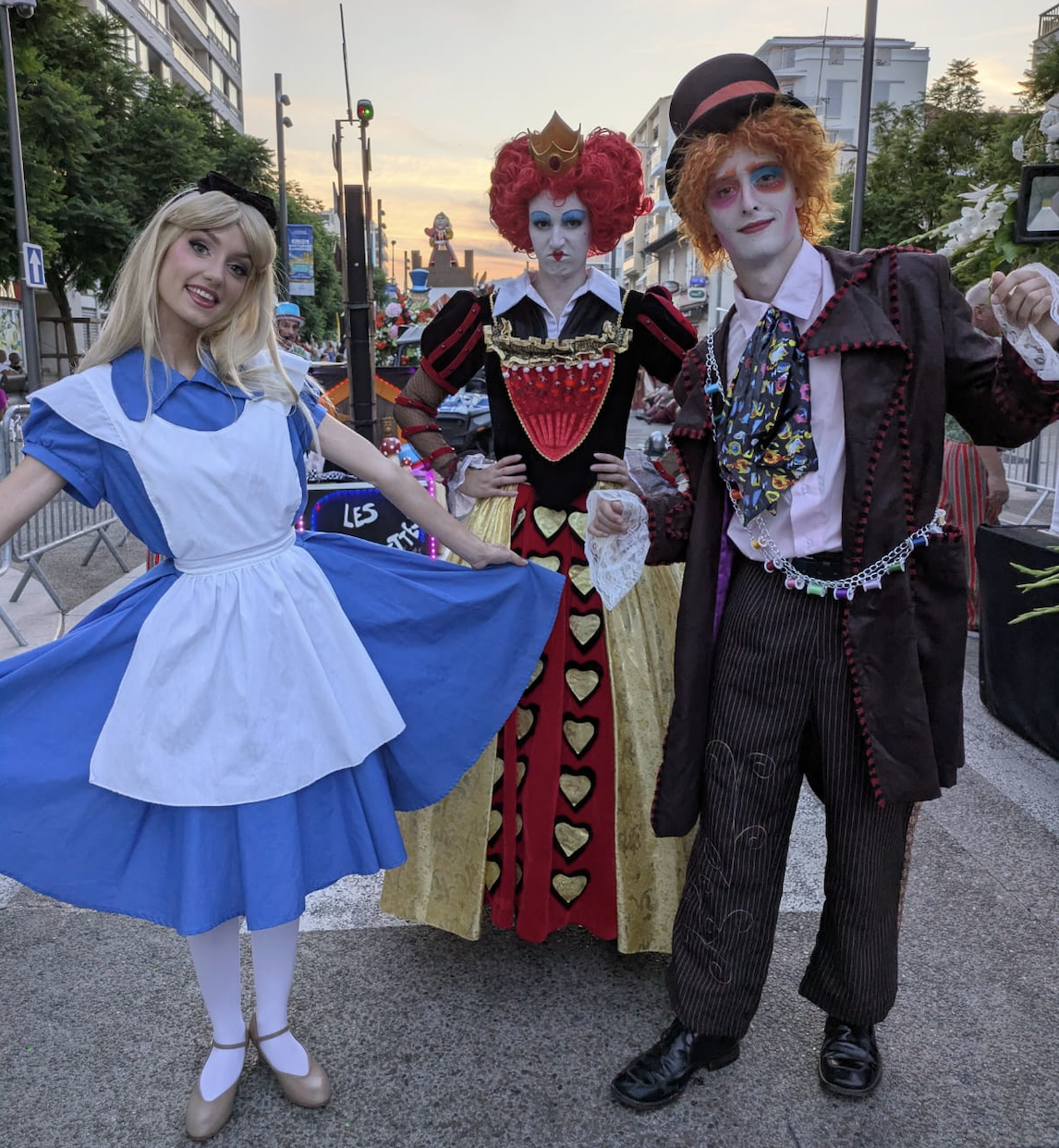 Trois personnes déguisées en personnages de conte ou de folie, probablement pour un carnaval ou une fête, posant dans une rue en soirée.