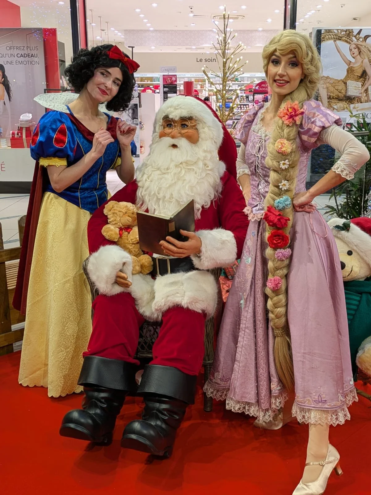 Des personnes déguisées en Blanche-Neige et Raiponce aux côtés du Père Noël dans un magasin de Noël.