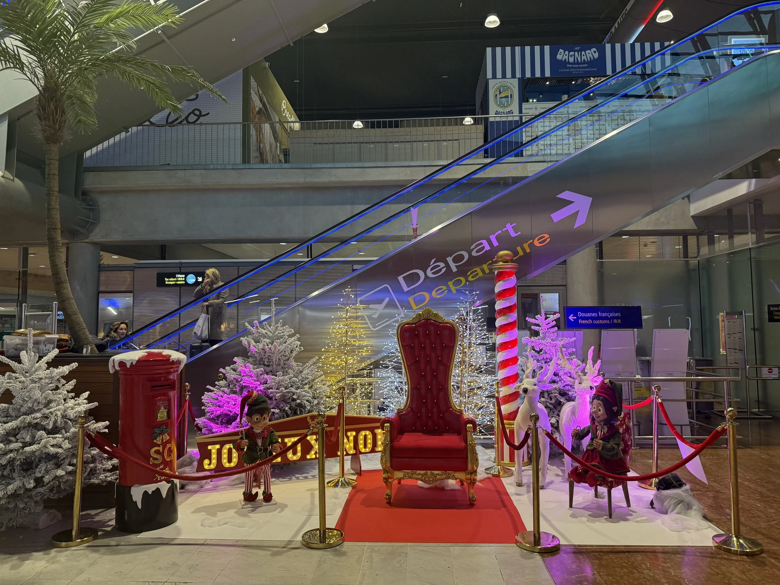 
Décorations de Noël dans un aéroport, avec un trône rouge, des sapins de Noël enneigés, des soldats de plomb, des rennes et des décorations festives.